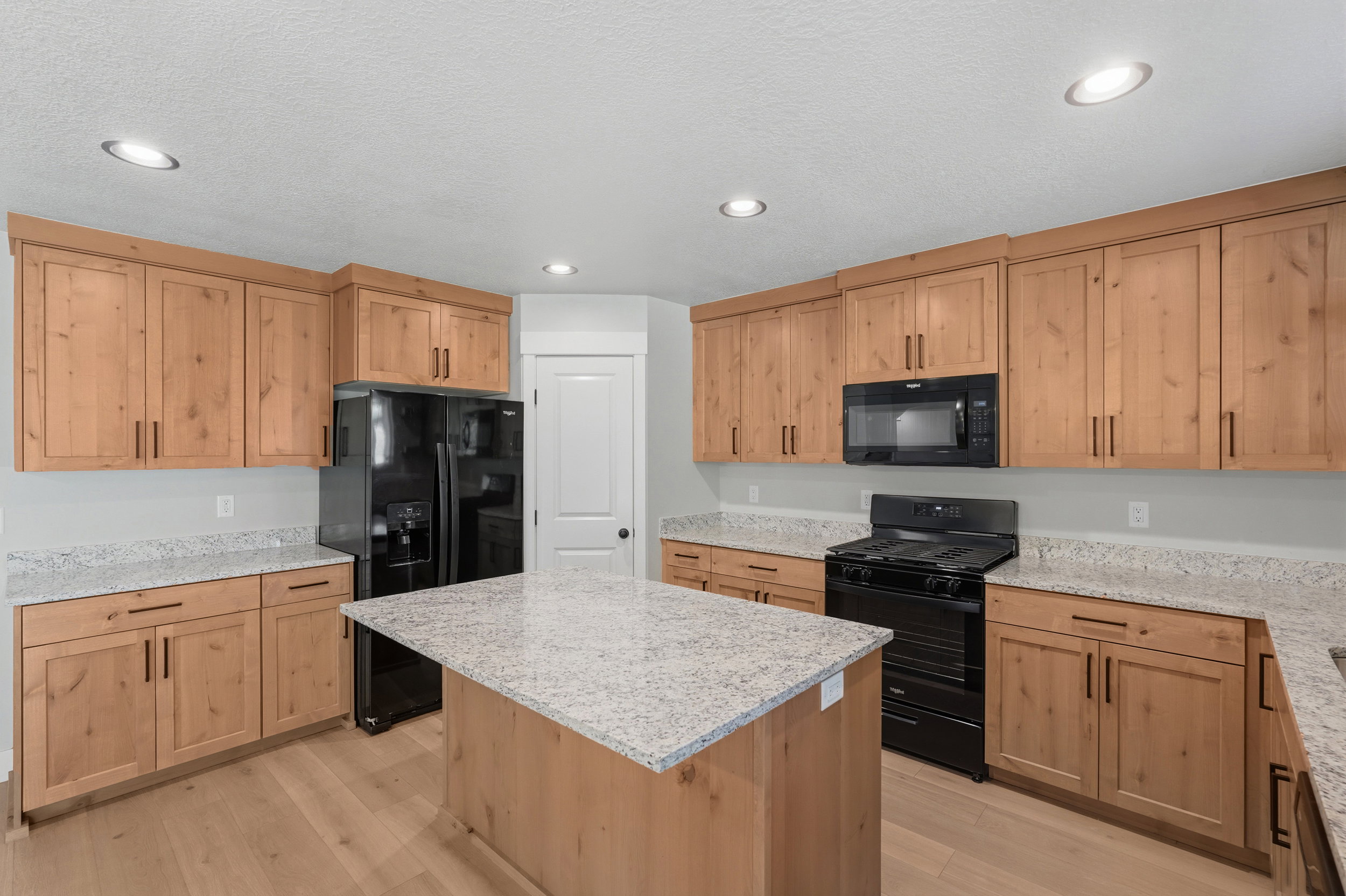 Kitchen featuring a central island, light wood-finish cabinetry, light speckled countertops, and black appliances