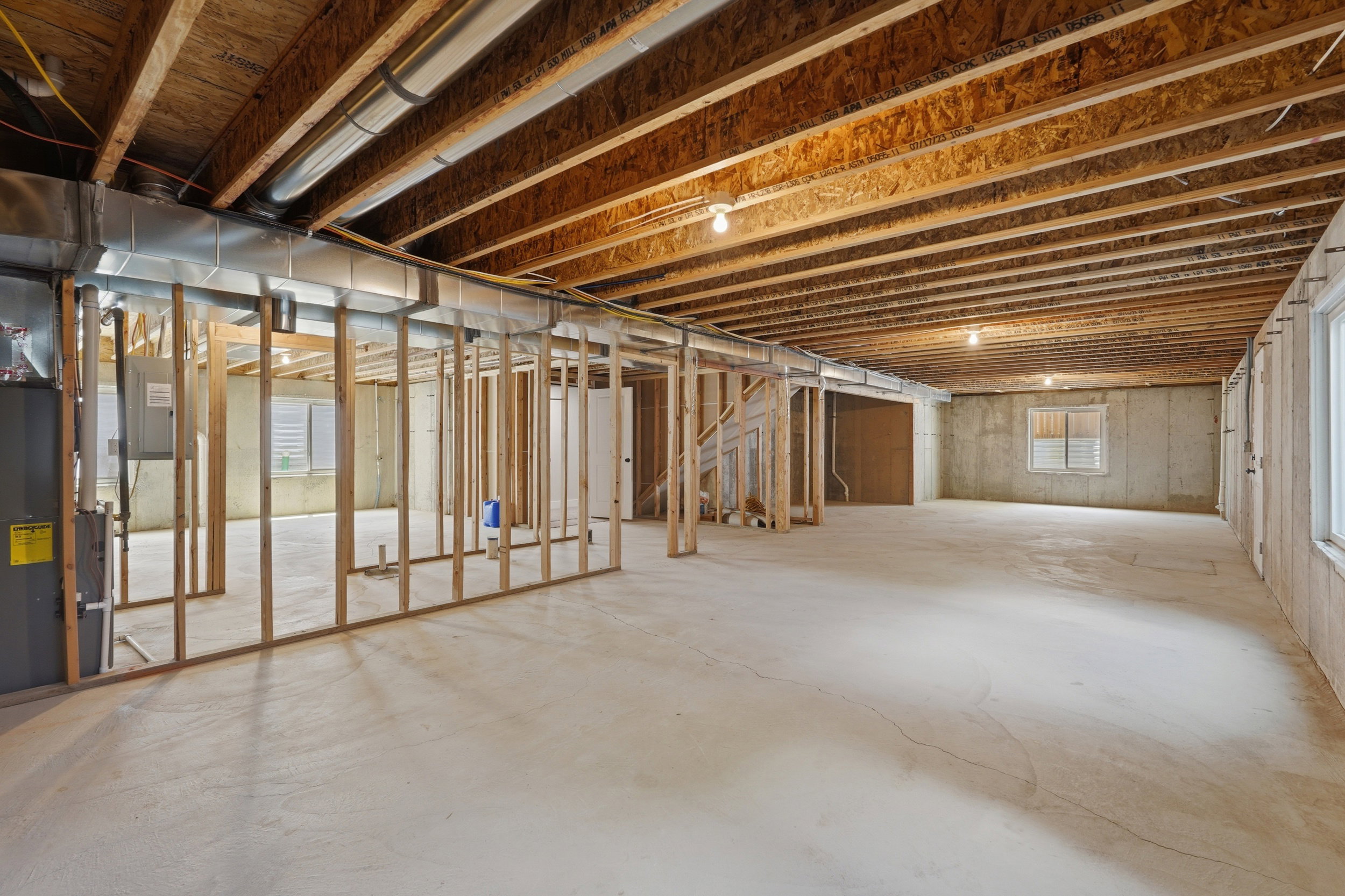 Unfinished lower level featuring exposed wood joists, concrete flooring, window wells, partial wood framing, and visible ductwork