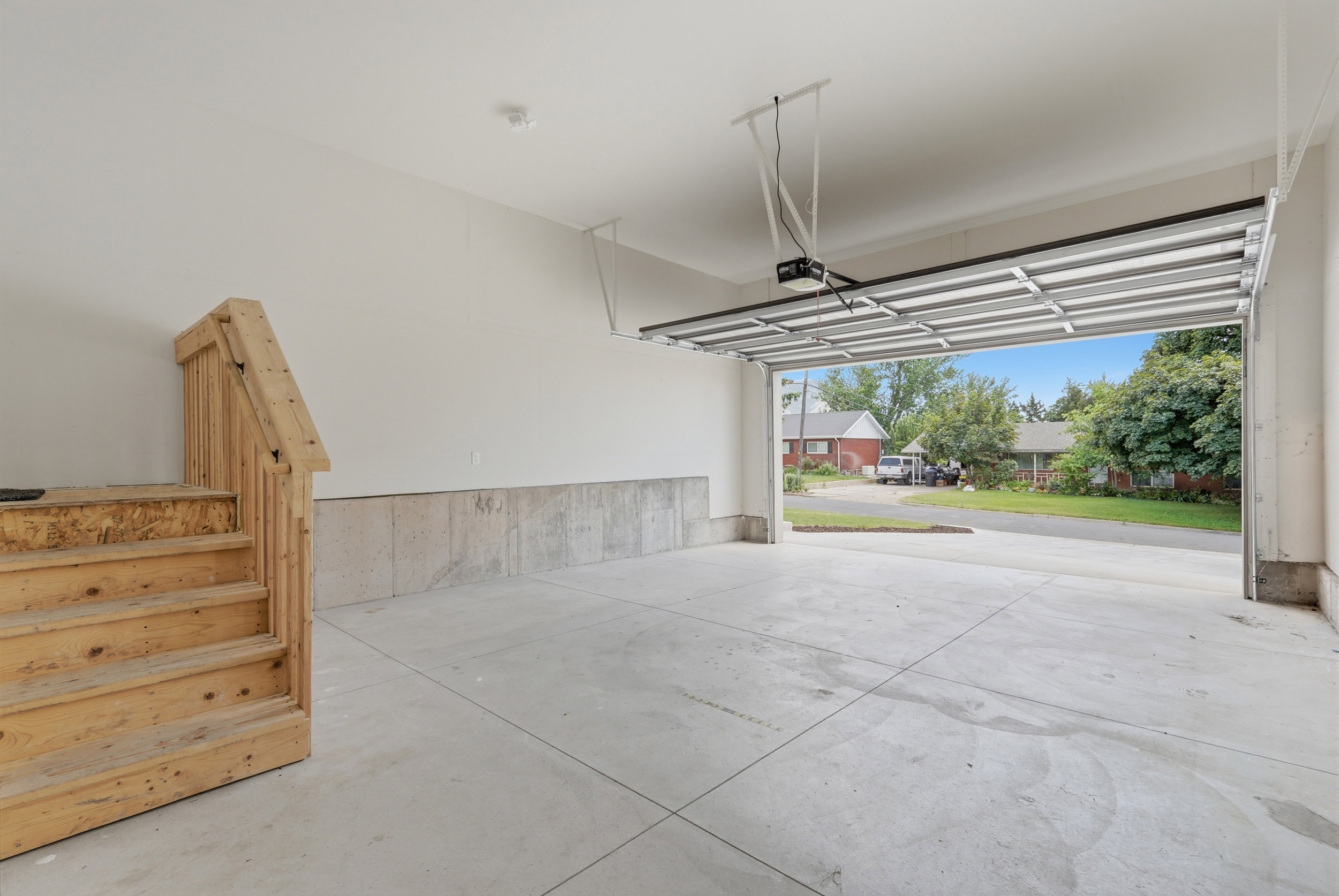 Spacious garage with an open overhead door, concrete flooring, and a built-in wooden staircase