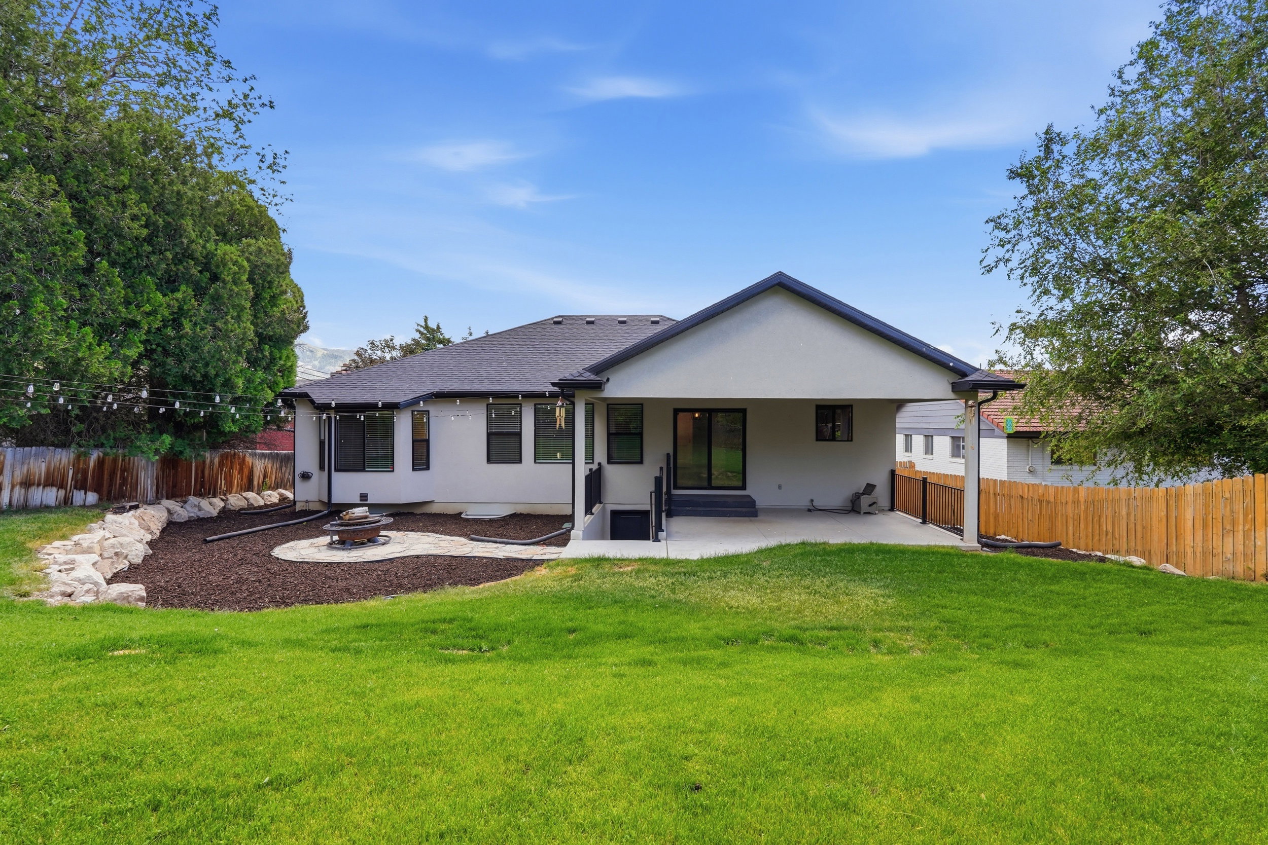 Back yard with covered patio, a recessed fire pit area with a stone border, and mature trees