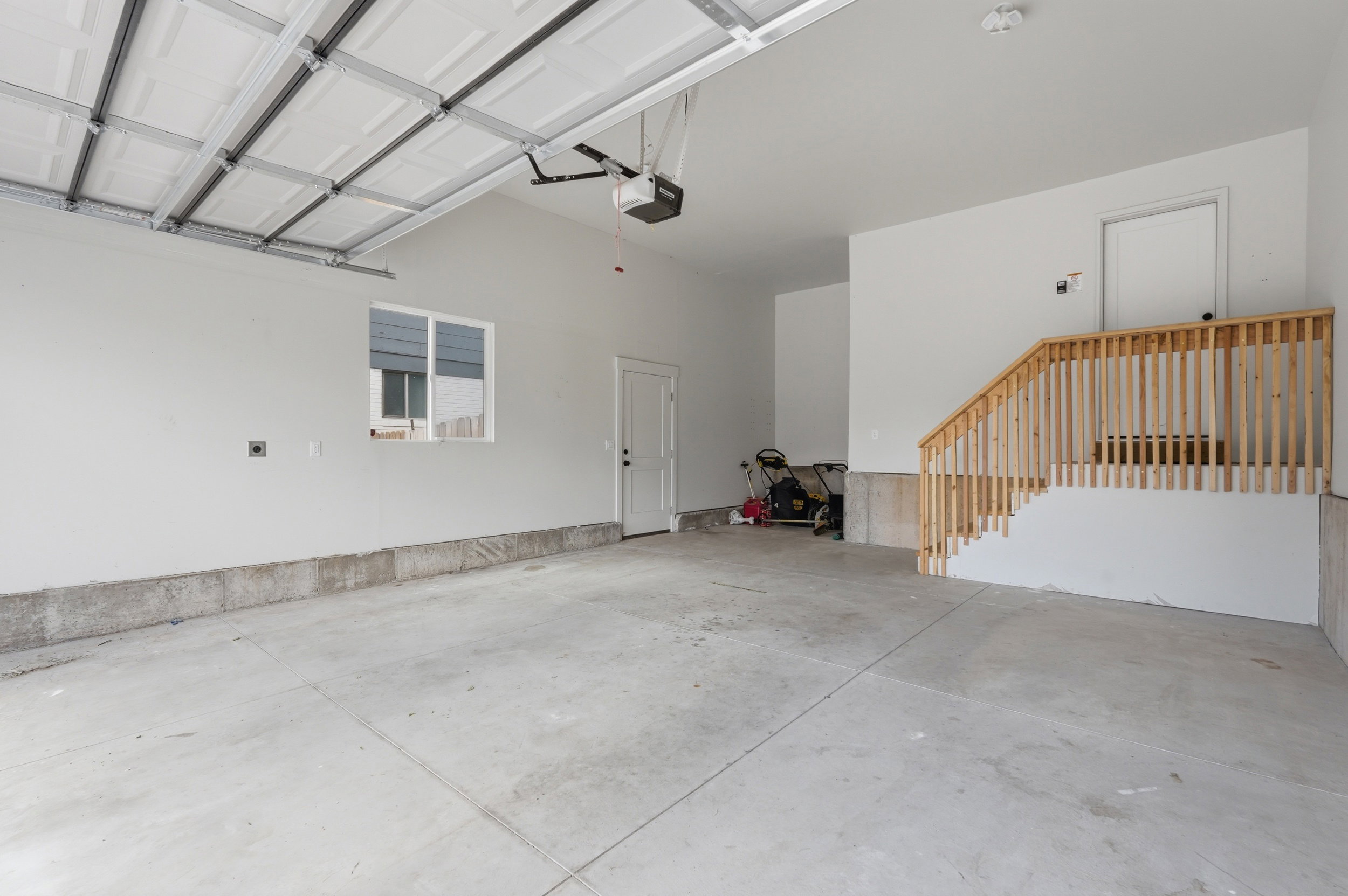 Spacious garage with concrete flooring, a single window, an interior access door, a garage door opener, and a wooden staircase