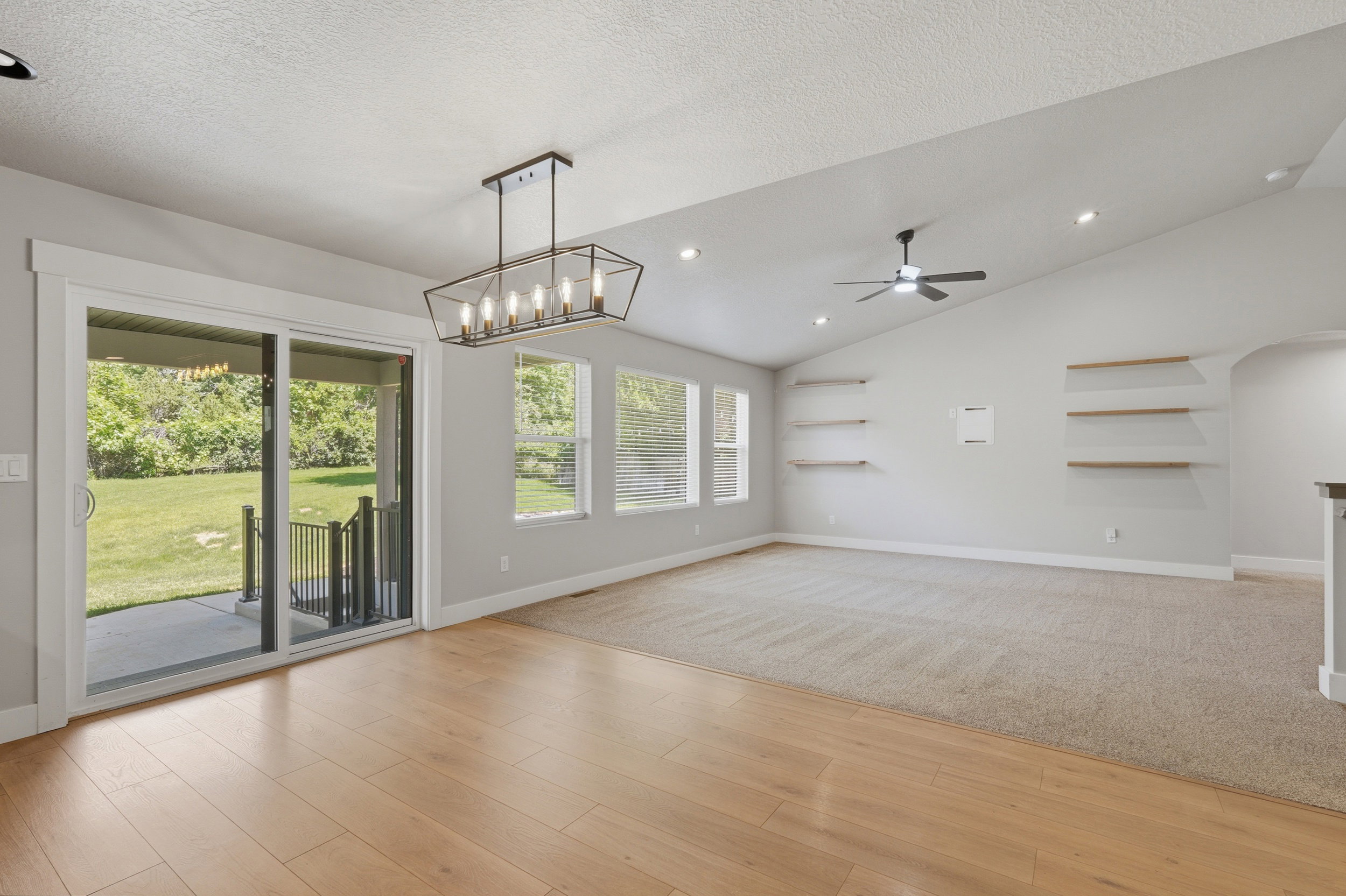 Open-concept living space featuring wood-finish flooring, a contemporary chandelier, vaulted ceilings, and a sliding glass door leading to an outdoor patio with a green yard beyond