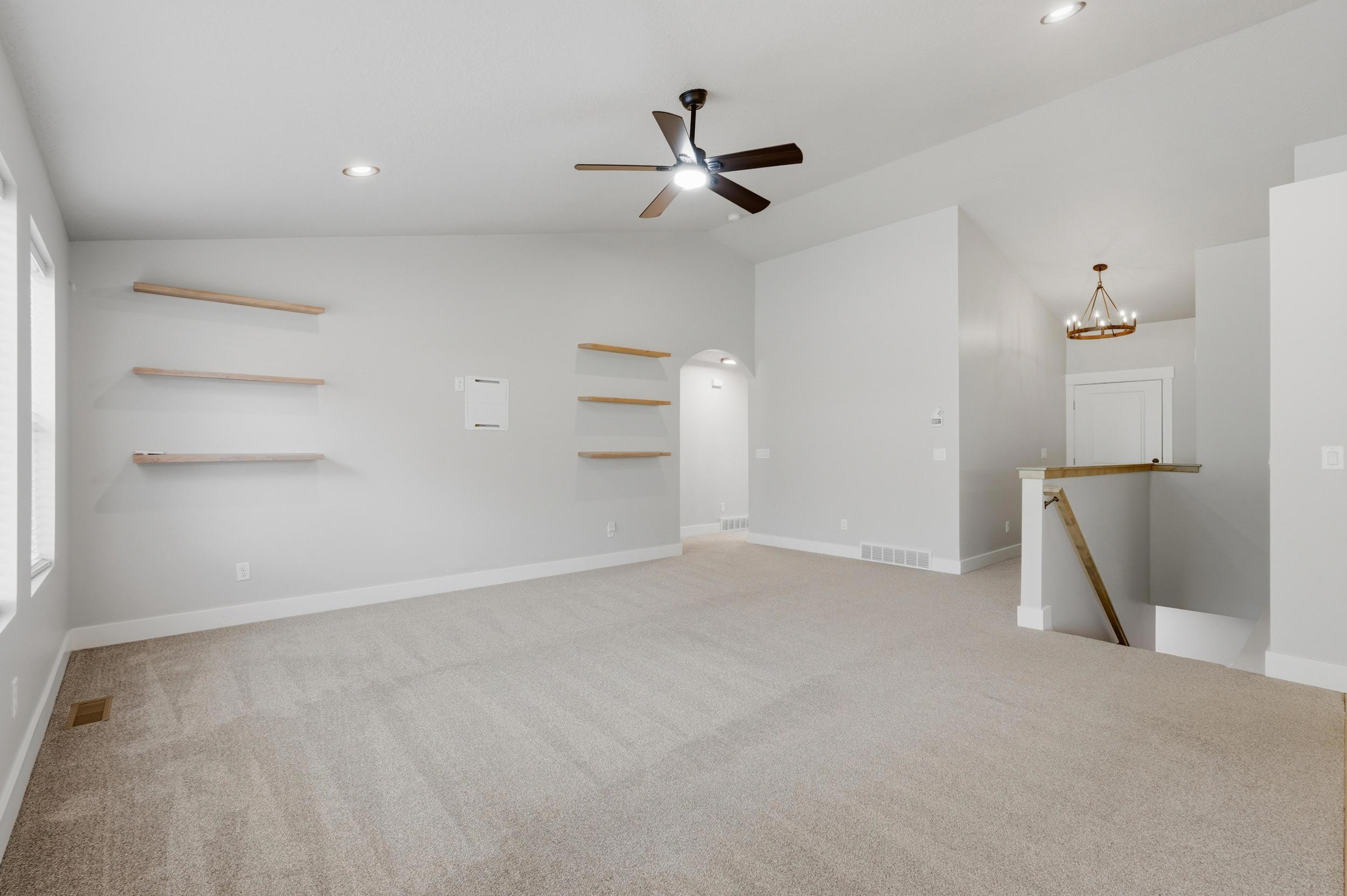 Carpeted living area featuring vaulted ceilings, recessed lighting, a ceiling fan, and built-in floating shelves