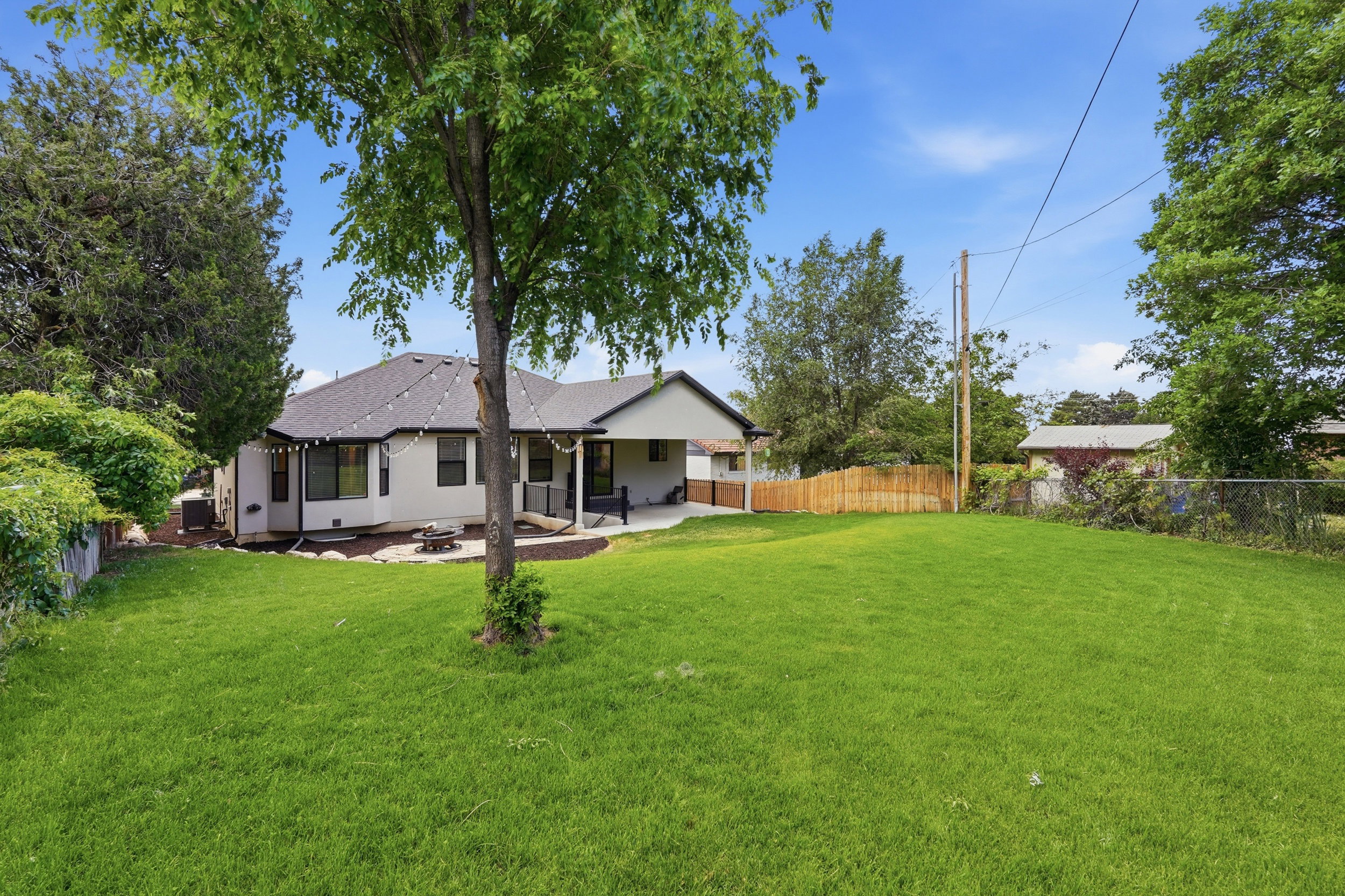 Expansive backyard featuring a large green lawn, concrete patio, and a covered patio area