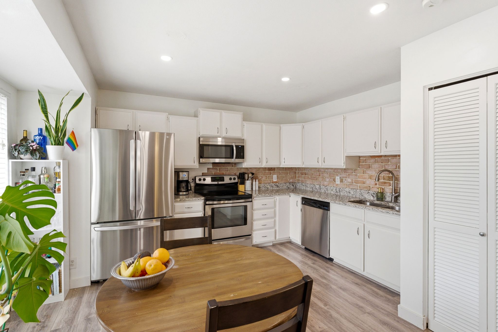 Kitchen featuring white cabinetry, stainless steel appliances, granite-style countertops, brick-style backsplash, and wood-finish flooring