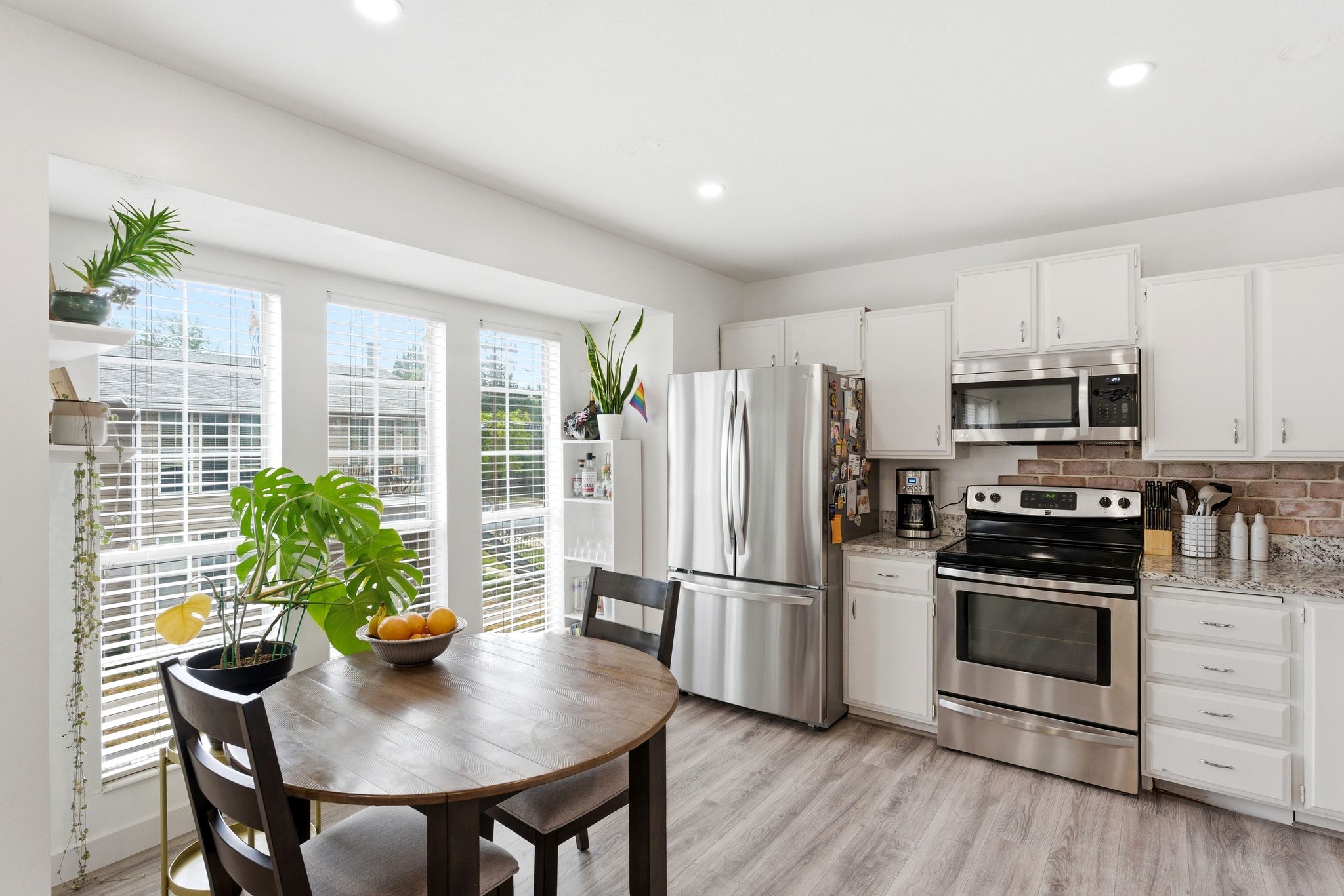 Bright kitchen featuring a bay window with multiple panes, stainless steel appliances, white cabinetry, granite-finish countertops, and wood-finish flooring