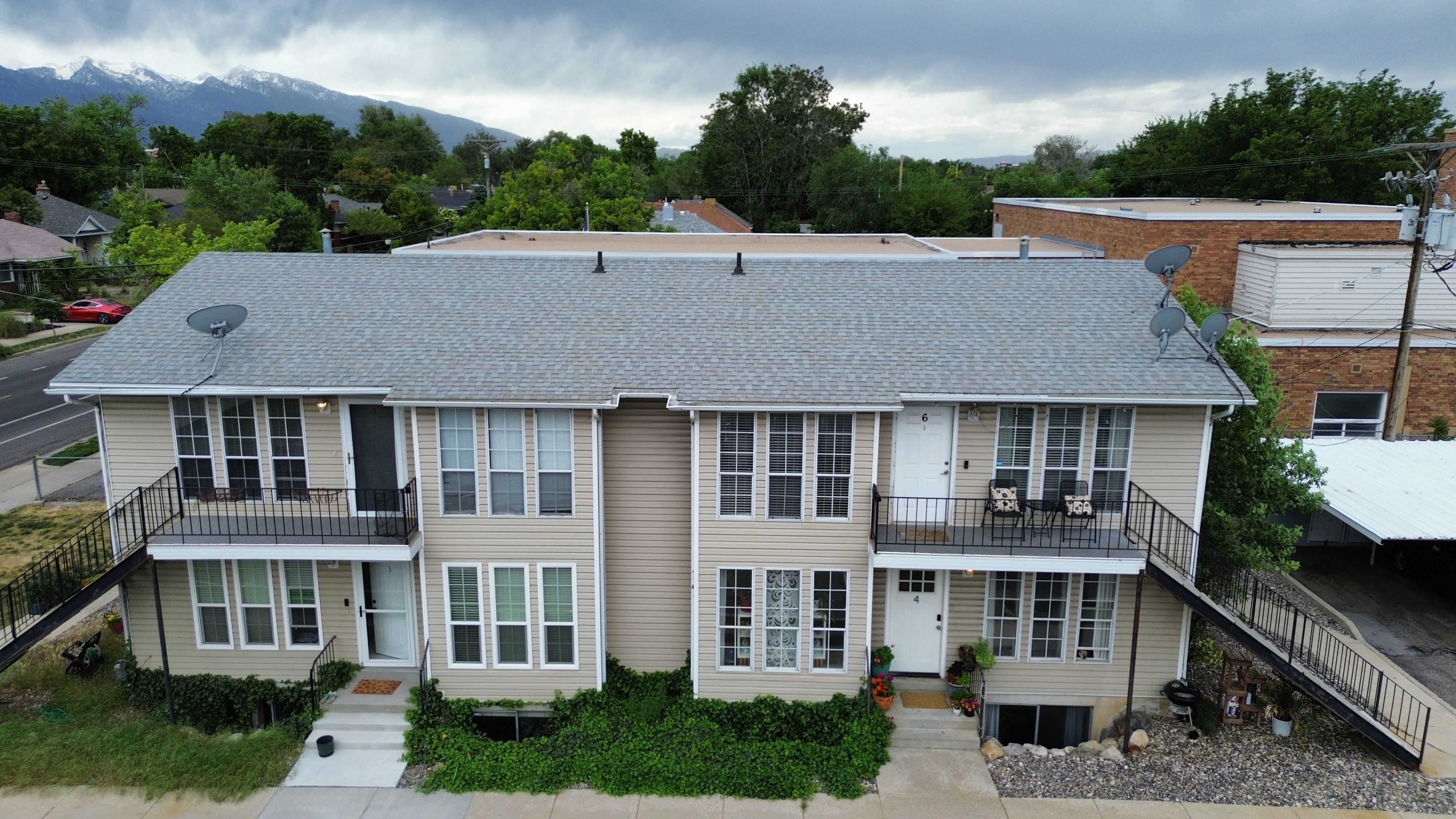 Multi-unit property featuring tan siding, a gray shingle roof, and multiple balconies with black railings