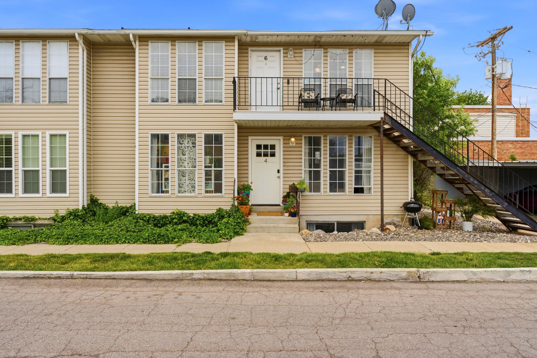 Exterior featuring light-toned horizontal siding, white-framed windows, and a black metal exterior staircase providing access to the upper-level balcony