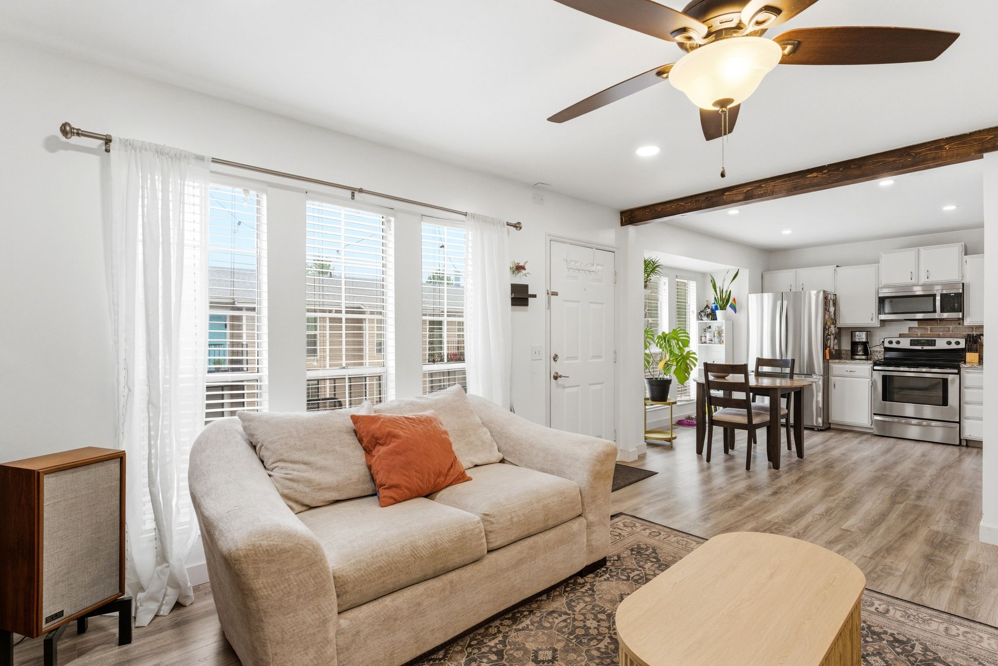 Open-concept living space featuring wood-finish flooring, a ceiling fan with integrated lighting, and multiple windows with blinds
