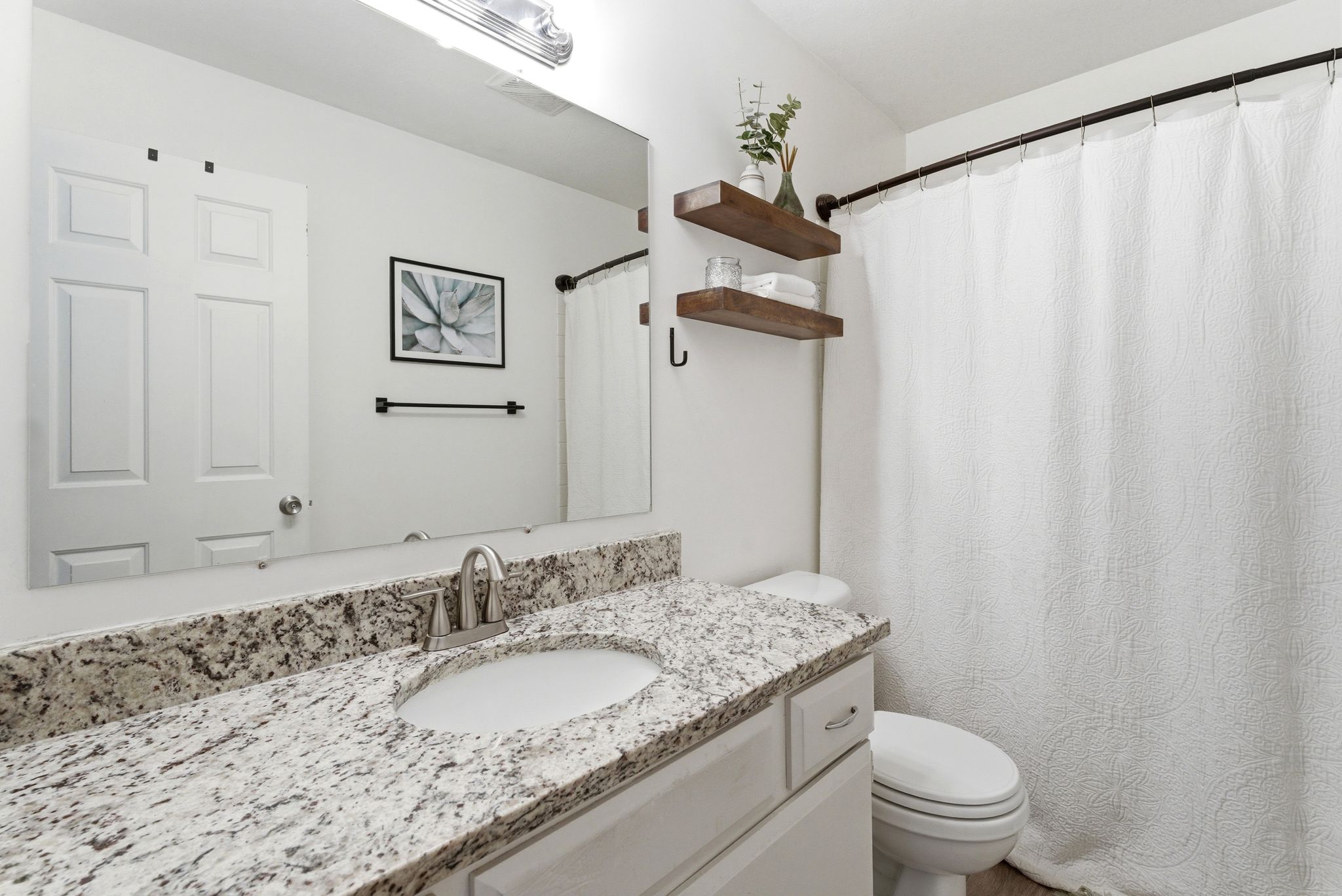 Bathroom featuring a granite-finish countertop with an undermount sink, brushed nickel faucet, and a large vanity mirror