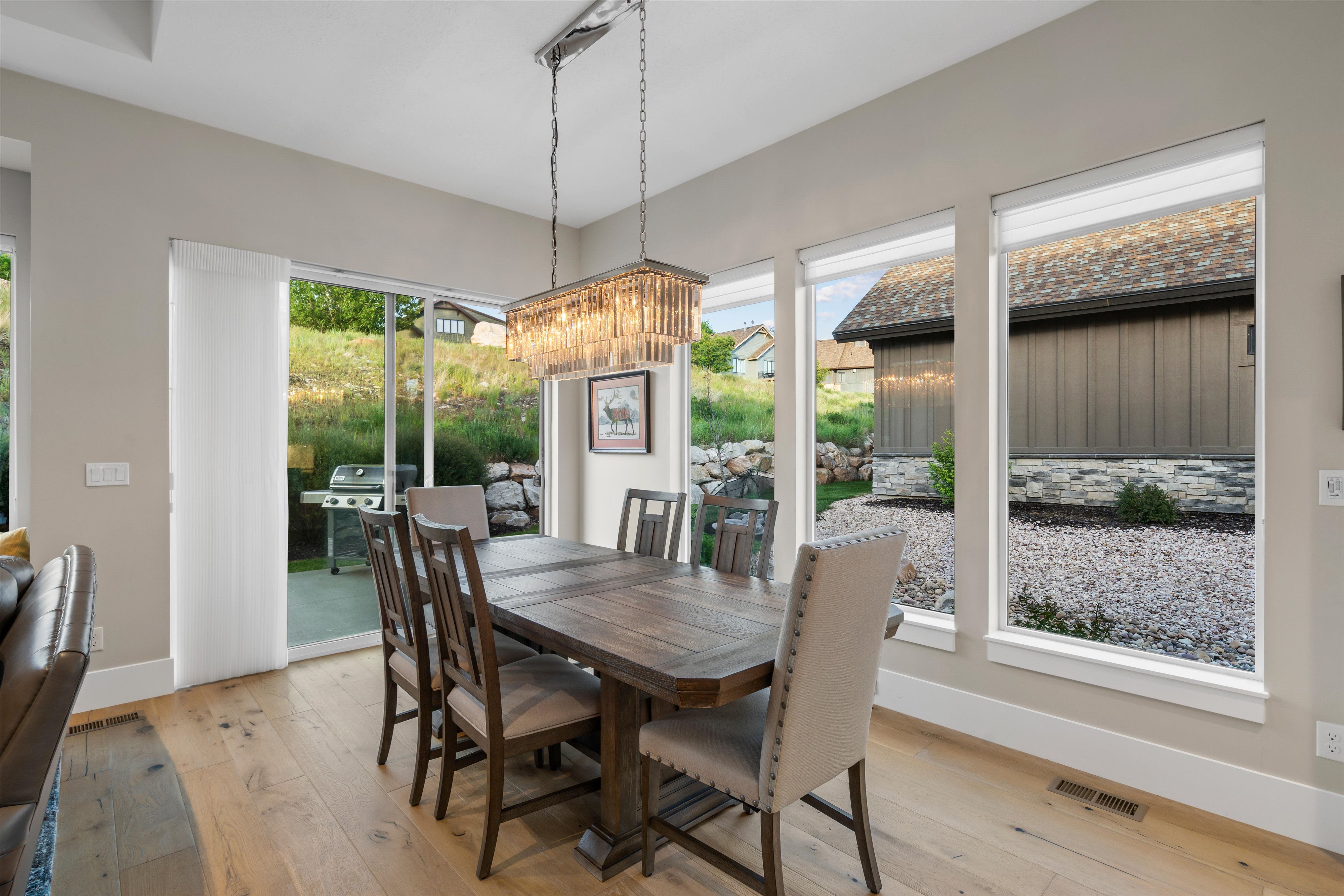 Dining area with wood-finish flooring, featuring a rectangular chandelier and expansive window array