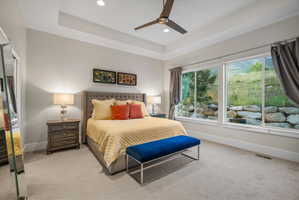 Spacious bedroom featuring large windows, tray ceiling, recessed lighting, and ceiling fan