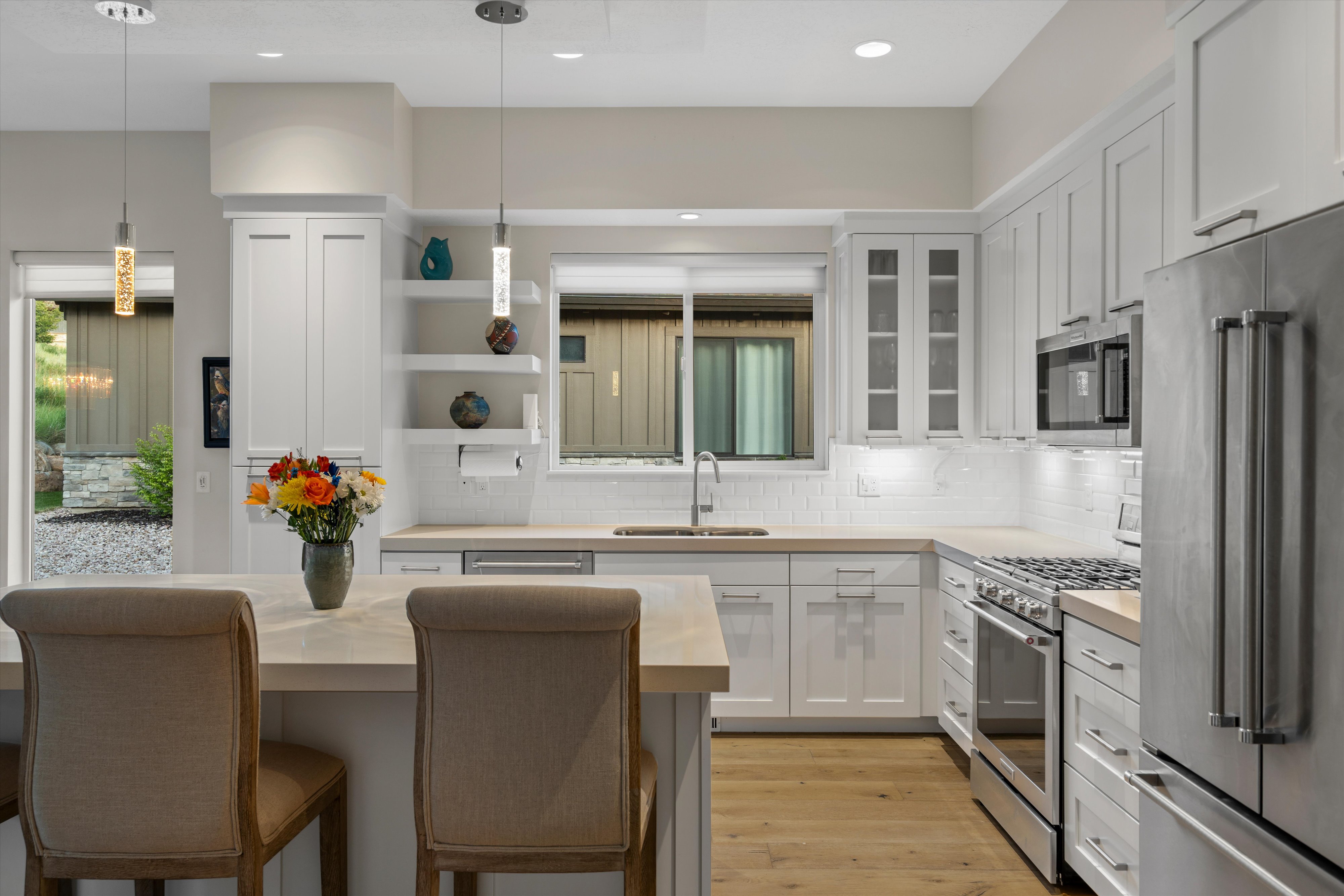 Modern kitchen featuring white shaker cabinetry, stainless steel appliances, light wood-finish flooring, a white subway tile backsplash, and a central island with pendant lighting