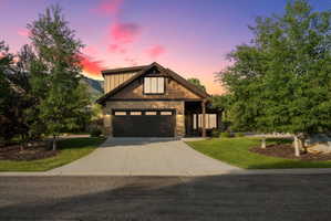 Craftsman-style exterior featuring a dark brown garage door, stone accents, wood siding, and gabled roofing