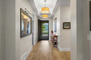 Entryway featuring wood-finish flooring, recessed ceiling with two drum pendant lights, and a dark-framed glass paneled door