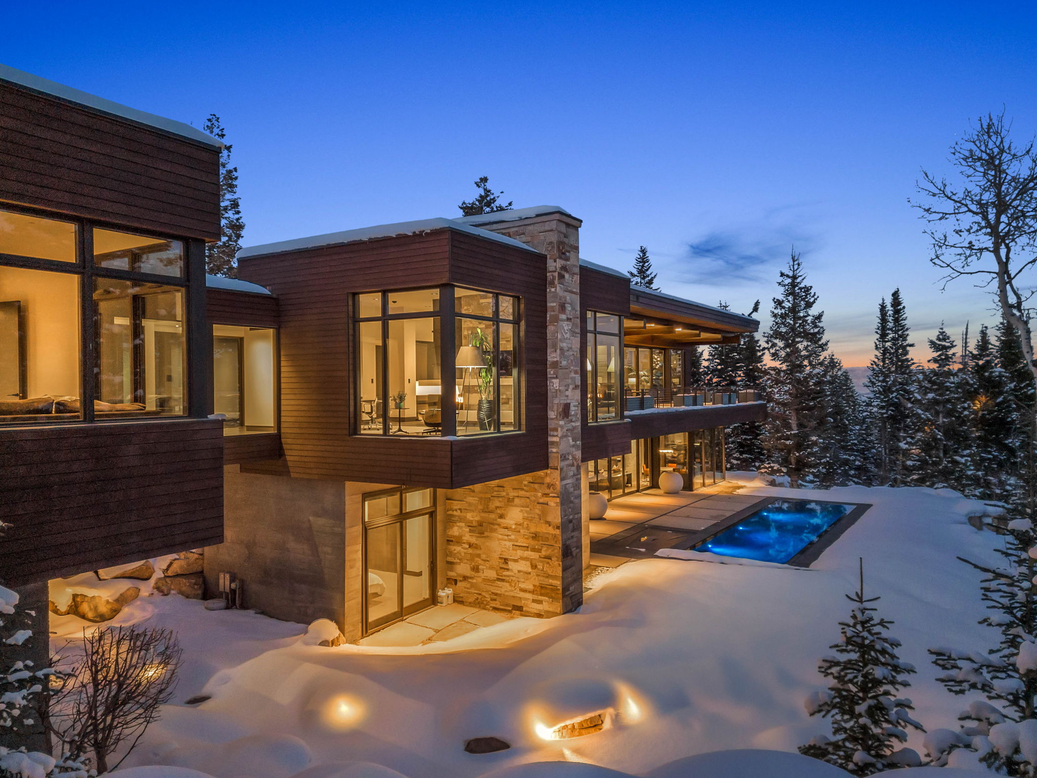 Modern exterior featuring rich wood paneling, extensive window walls, a stone pillar accent, an outdoor swimming pool, and a spacious patio area
