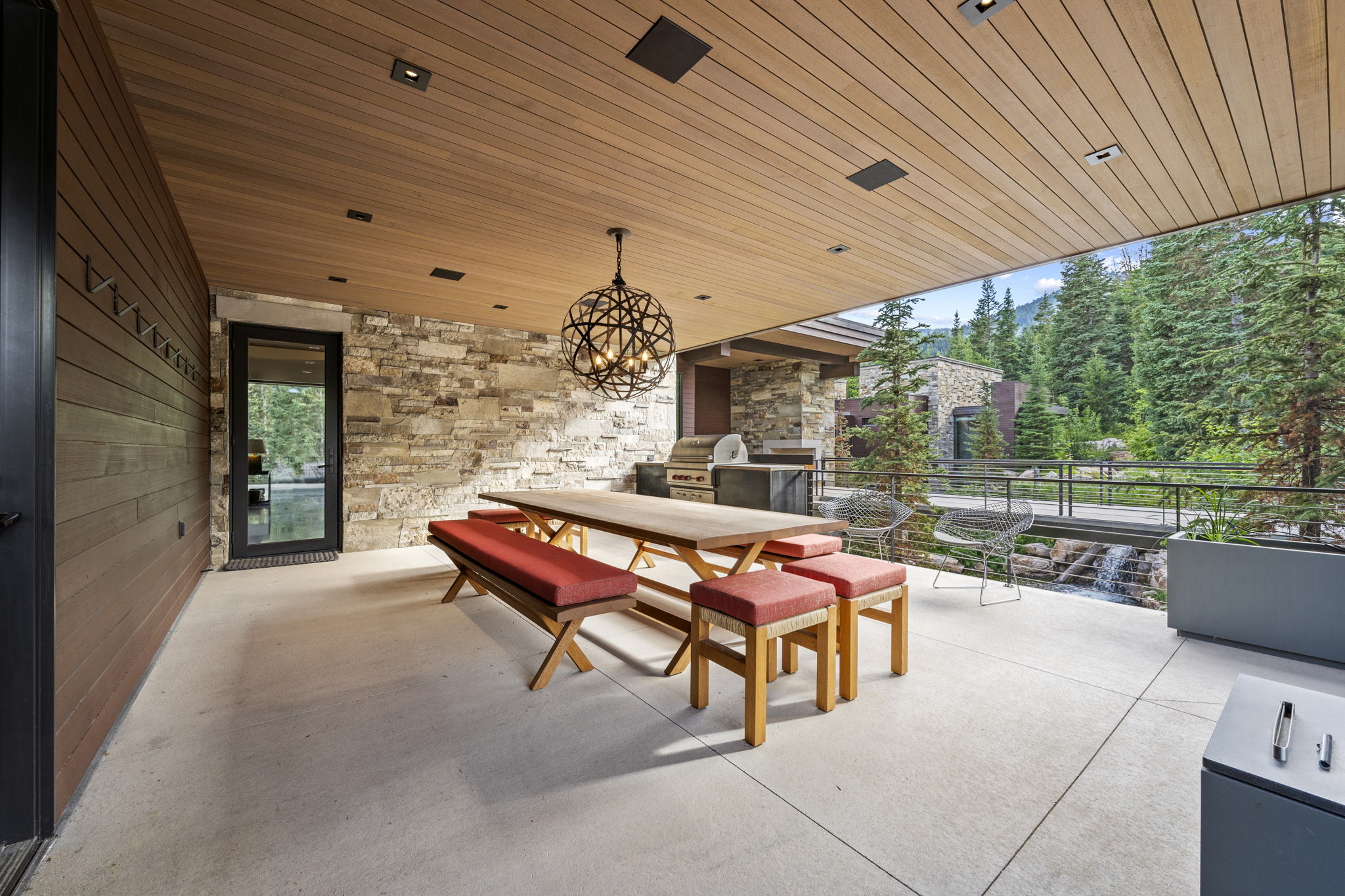Covered outdoor patio featuring a wood-finish ceiling with recessed lighting, a stone accent wall, an outdoor kitchen with built-in appliances, and a metal railing