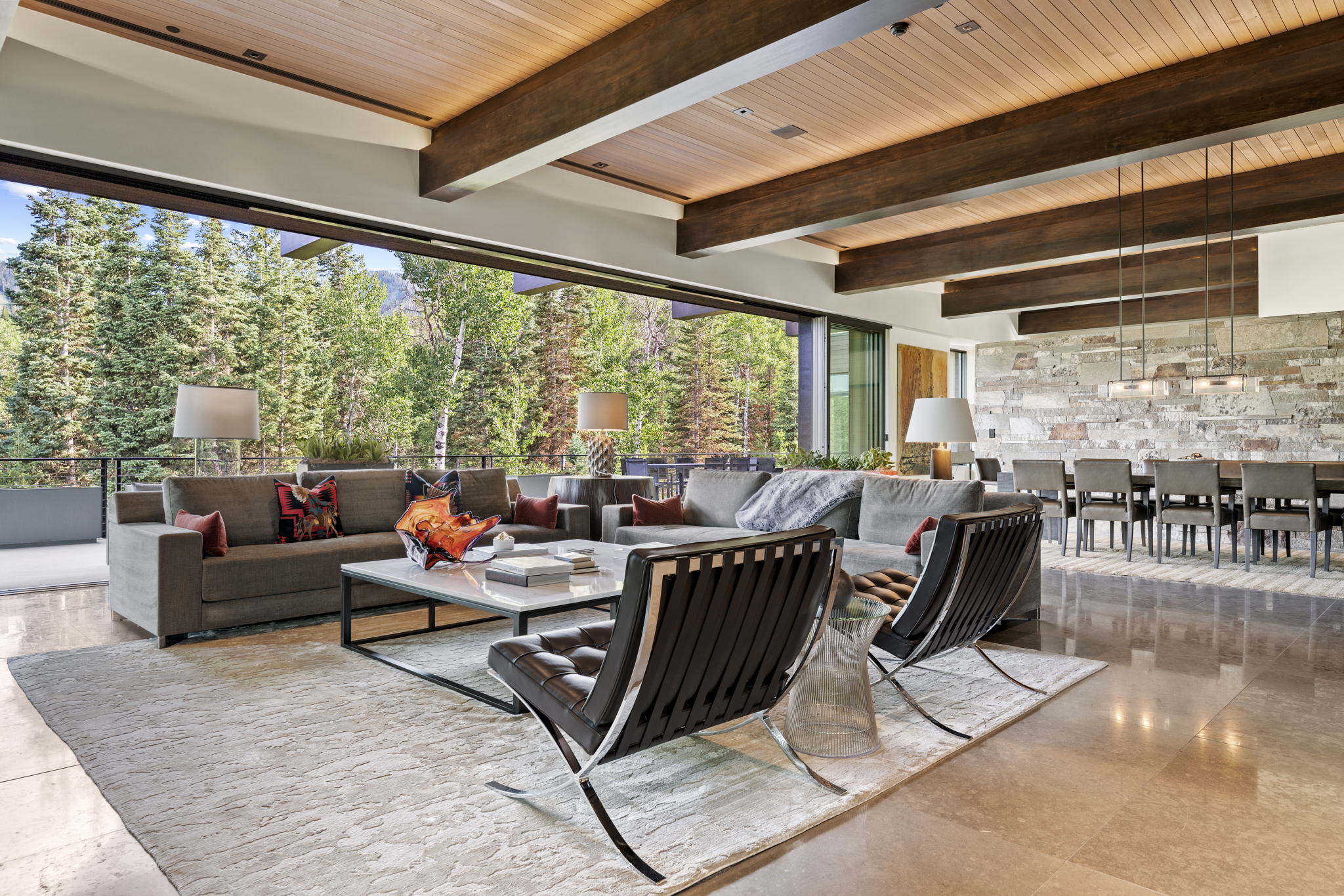 Expansive living area featuring a wood-panel ceiling with exposed beams, polished stone flooring, and a floor-to-ceiling retractable glass wall