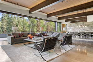 Expansive living area featuring a wood-panel ceiling with exposed beams, polished stone flooring, and a floor-to-ceiling retractable glass wall