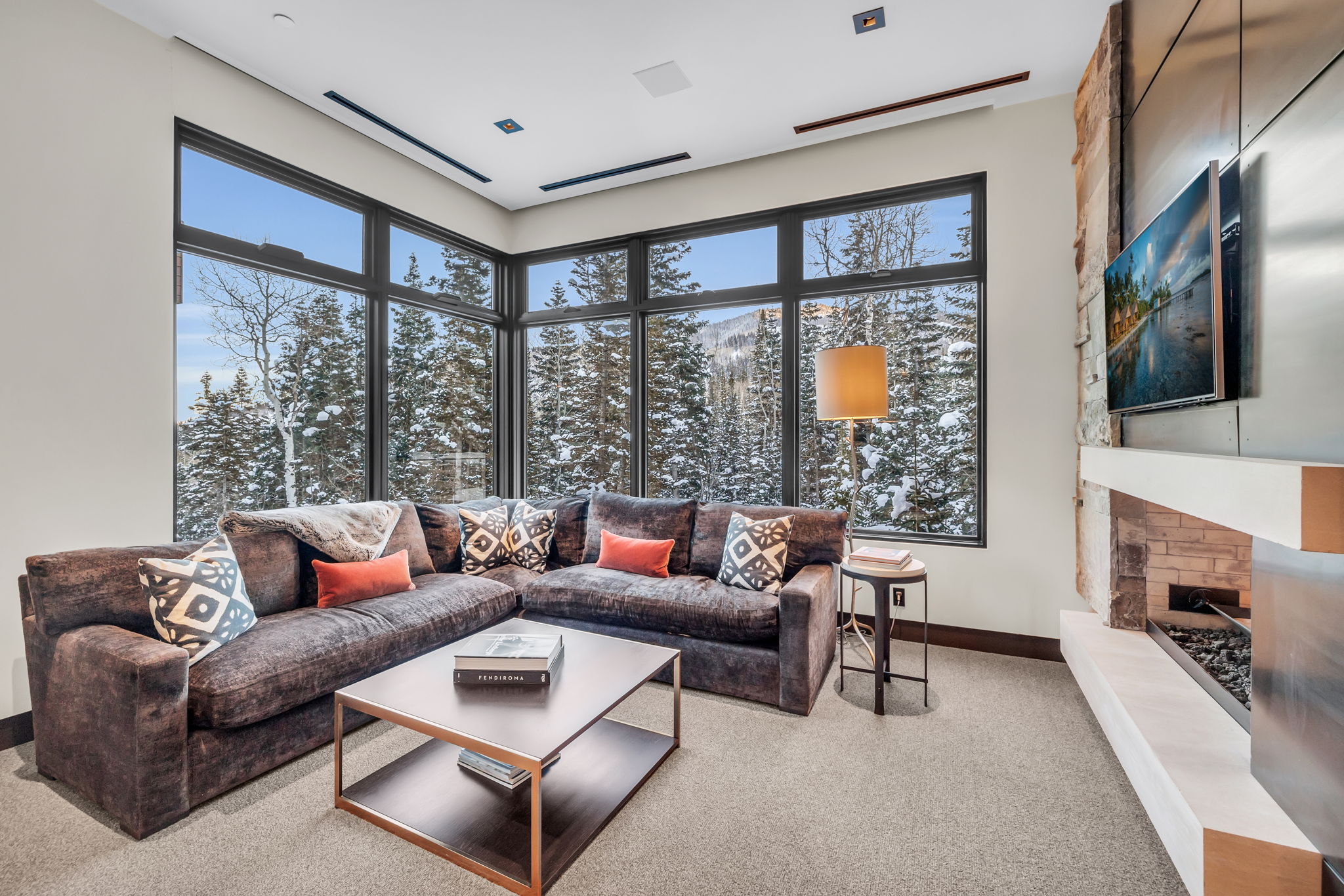 Spacious living area featuring extensive window walls, a linear fireplace with stone surround, a floating mantel, and high ceilings with recessed lighting