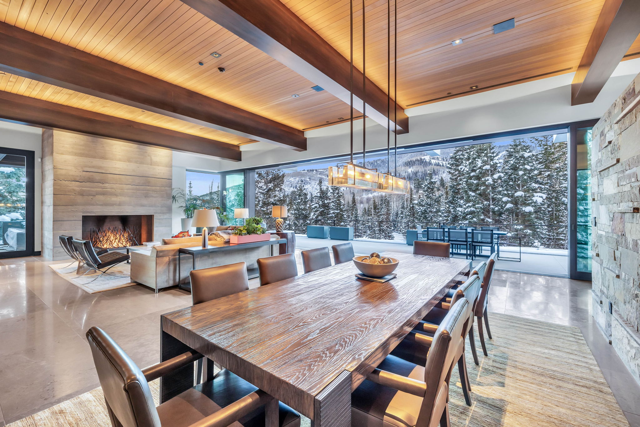 Spacious dining area featuring a long wooden table, a contemporary chandelier, and expansive windows