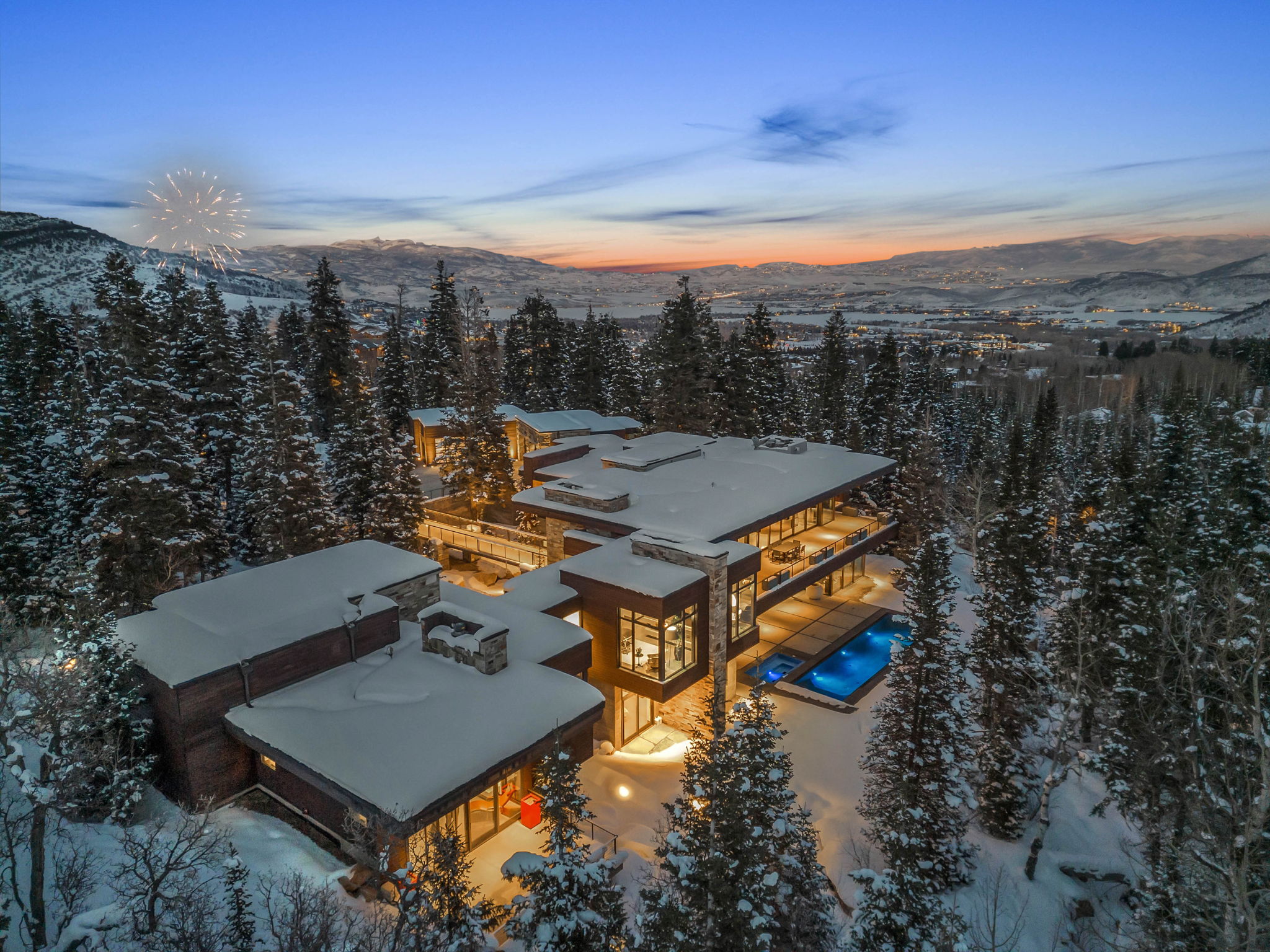 Expansive architectural residence featuring multiple outdoor terraces, large format windows, a stone exterior, and an illuminated outdoor pool