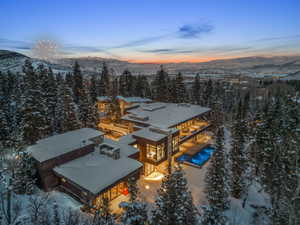 Expansive architectural residence featuring multiple outdoor terraces, large format windows, a stone exterior, and an illuminated outdoor pool