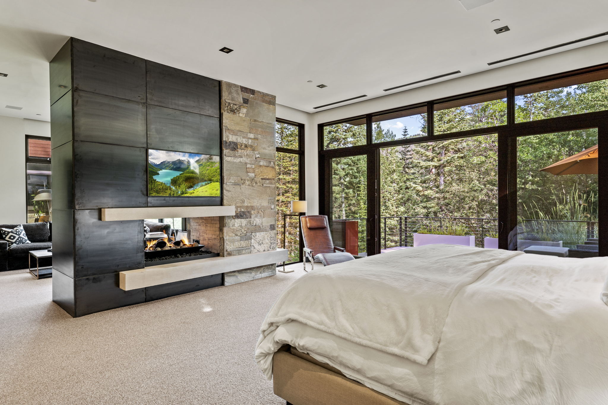 Floor-to-ceiling windows with expansive glass, a stone and metal fireplace feature, gas fireplace, light-toned carpet flooring, and a recessed ceiling