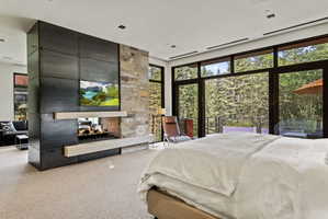 Floor-to-ceiling windows with expansive glass, a stone and metal fireplace feature, gas fireplace, light-toned carpet flooring, and a recessed ceiling