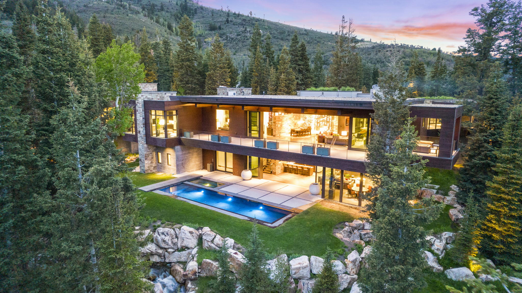 Modern architectural residence featuring extensive glass facades, multiple outdoor balconies, a rectangular swimming pool, and a structured outdoor patio space