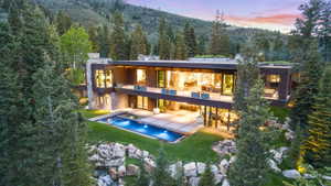 Modern architectural residence featuring extensive glass facades, multiple outdoor balconies, a rectangular swimming pool, and a structured outdoor patio space