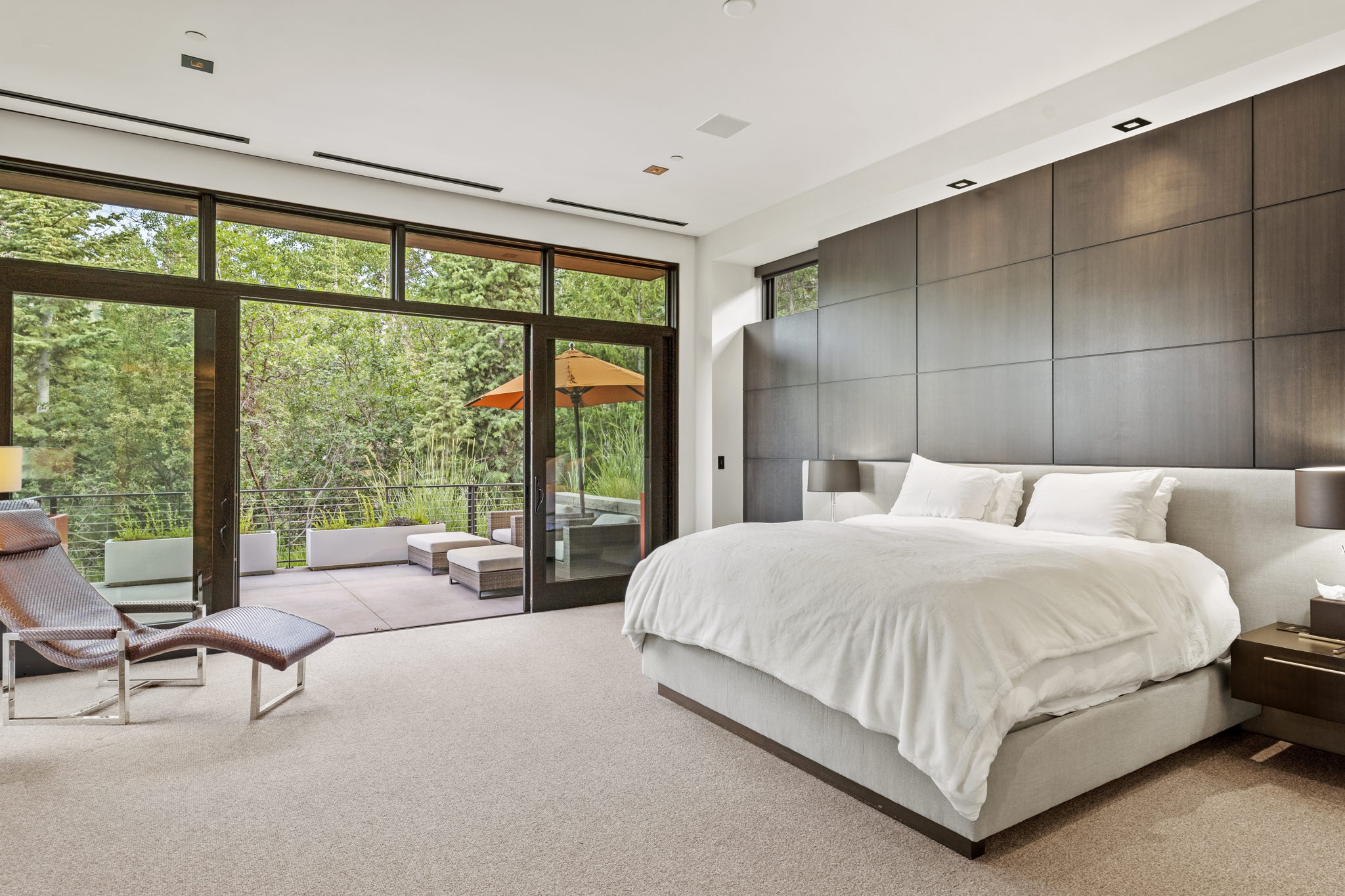 Expansive bedroom featuring a floor-to-ceiling glass wall with sliding doors leading to an outdoor patio
