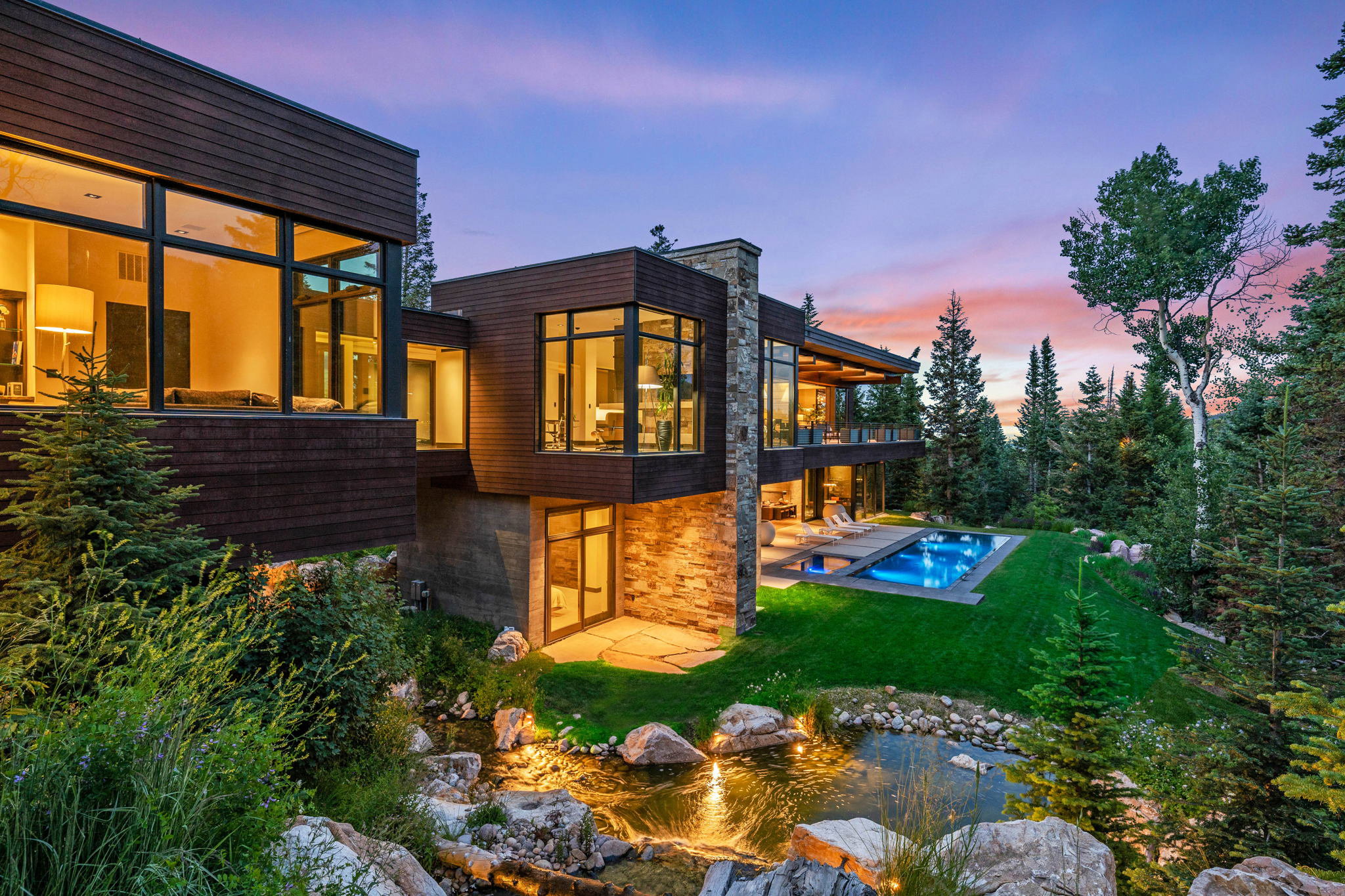 Modern mountain architecture featuring a multi-level design with extensive glass windows, stacked stone accents, and wood siding