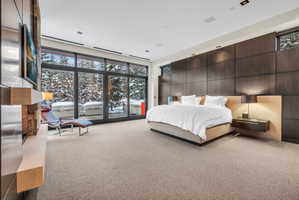 Floor-to-ceiling windows with dark frames, a built-in stone fireplace feature, dark wood paneling, and a light-toned carpet