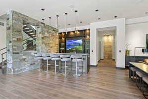 Built-in bar with pendant lighting, stone accents, and wood-finish flooring
