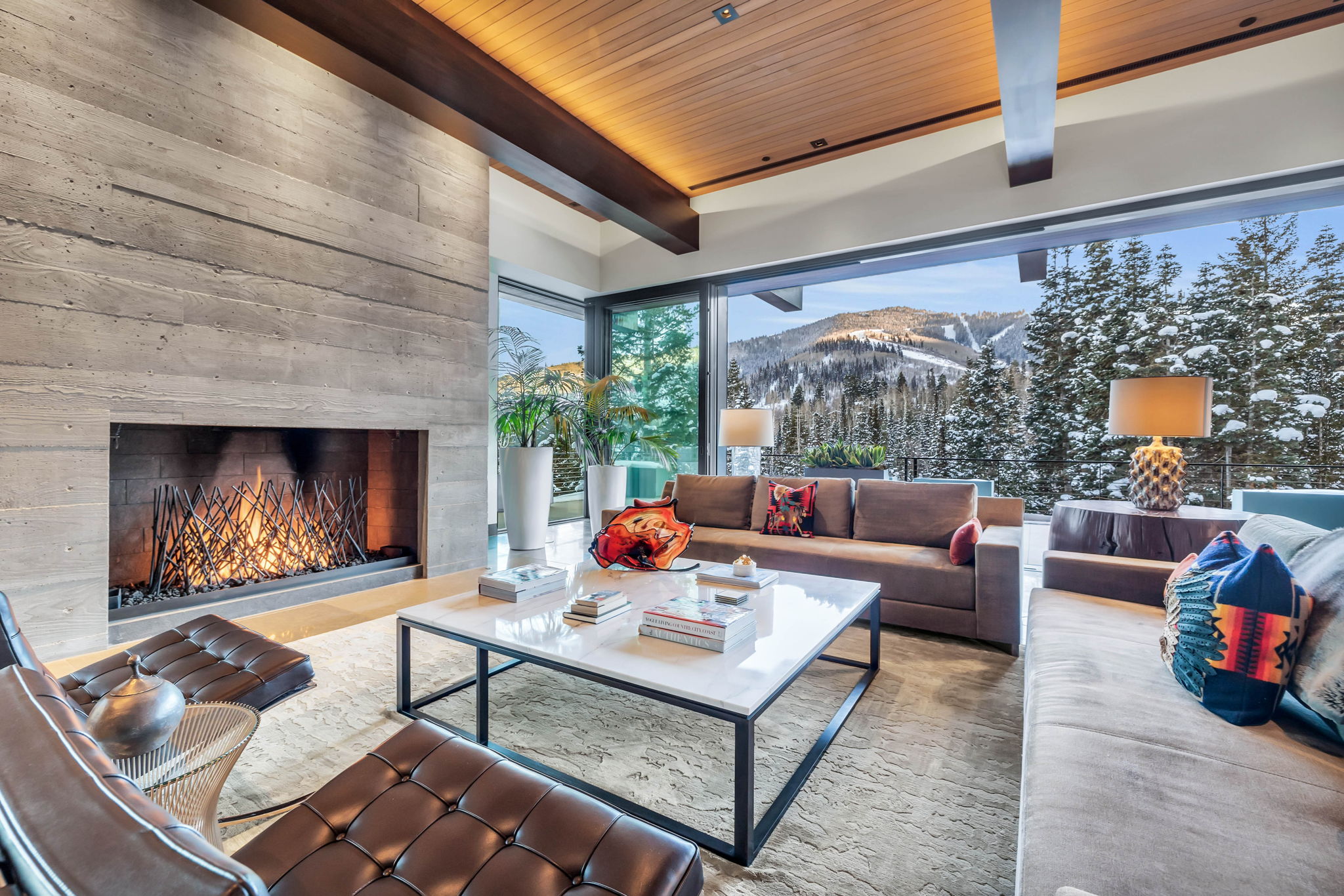 Living area featuring a board-formed concrete fireplace, full-height sliding glass doors, a wood-paneled ceiling, and exposed structural beams
