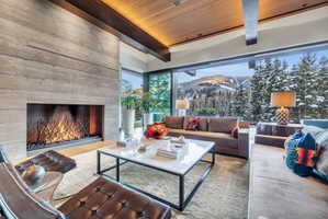 Living area featuring a board-formed concrete fireplace, full-height sliding glass doors, a wood-paneled ceiling, and exposed structural beams