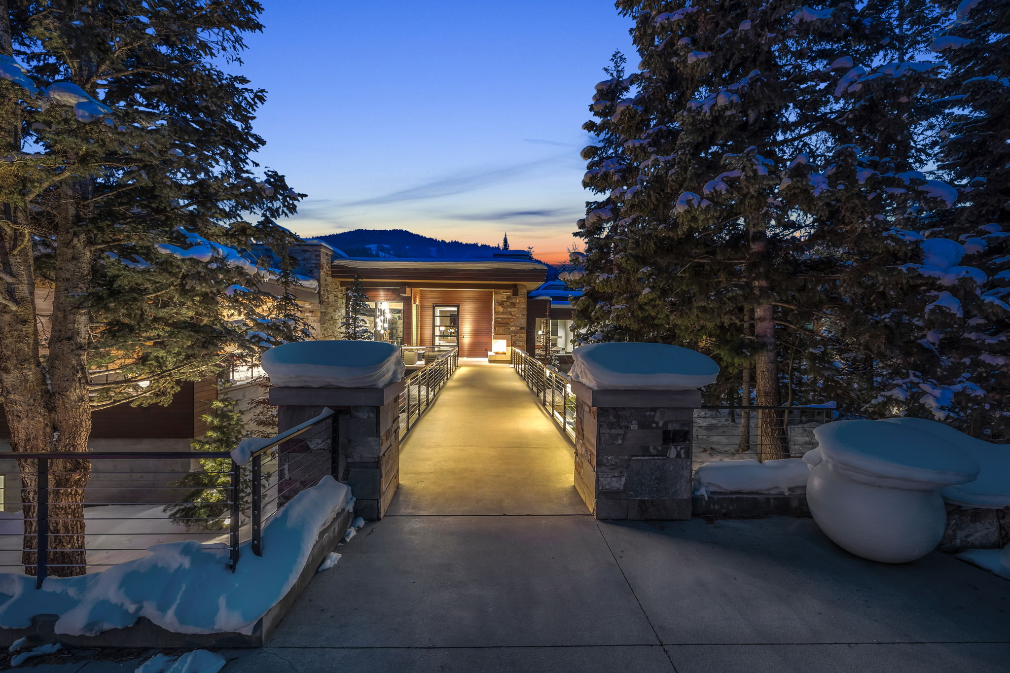 Illuminated entrance pathway featuring stone pillars and metal railings