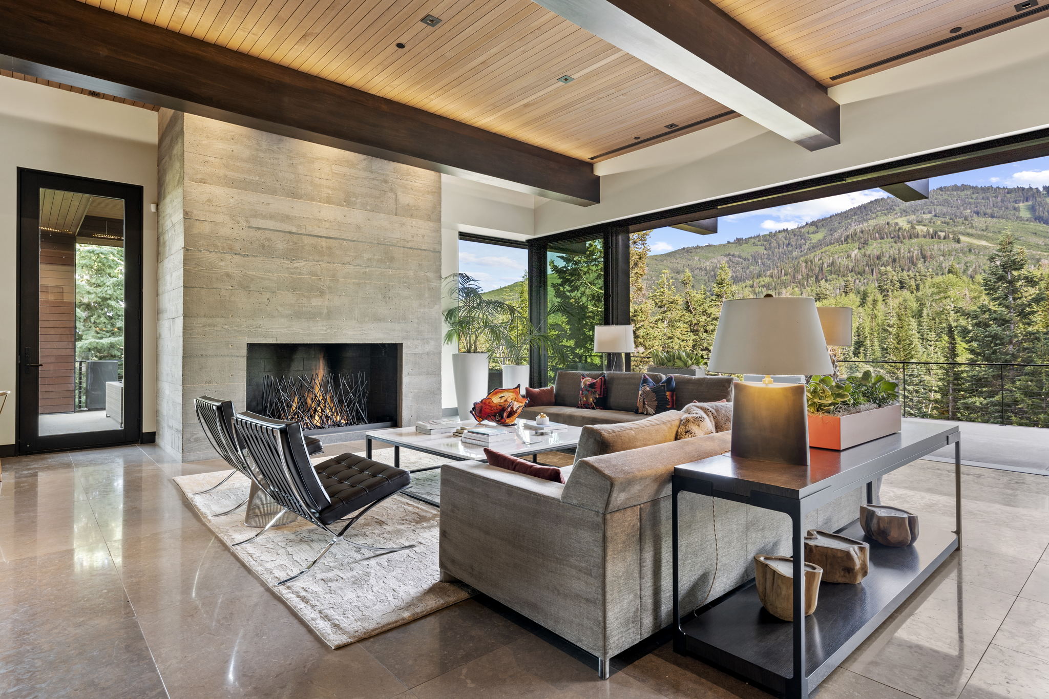 Spacious living area featuring a board-formed concrete fireplace, a wood-paneled ceiling with dark wood beams, and large format polished tile flooring