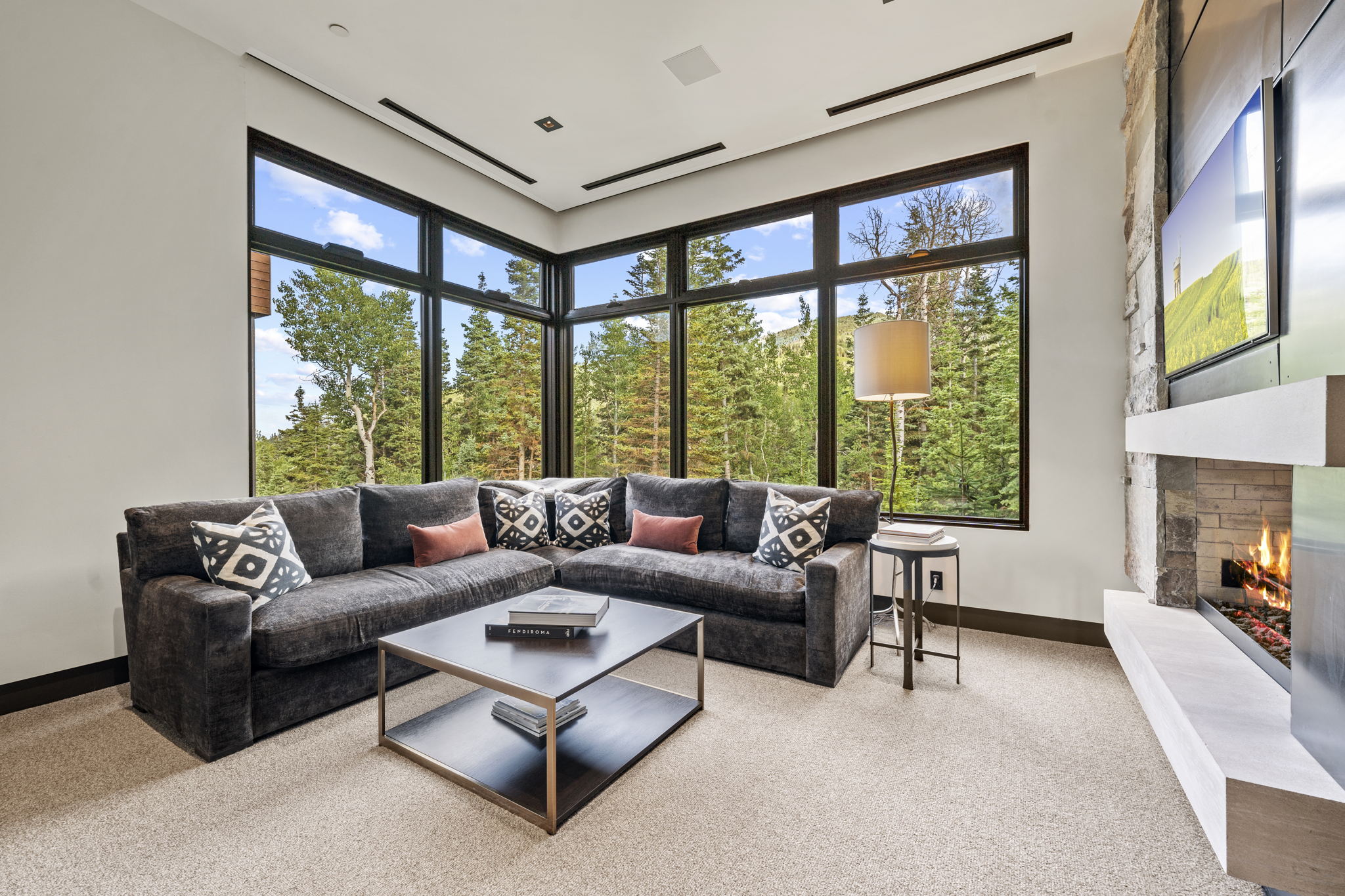 Floor-to-ceiling windows, a stone-clad fireplace with a hearth, recessed ceiling lighting, and dark trim details