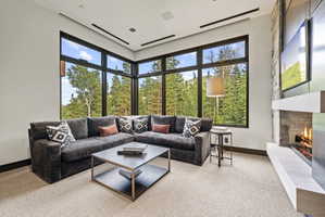 Floor-to-ceiling windows, a stone-clad fireplace with a hearth, recessed ceiling lighting, and dark trim details