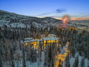 Extensive property nestled among snow-covered evergreen trees, featuring multiple levels, numerous illuminated windows, and a multi-peaked roofline