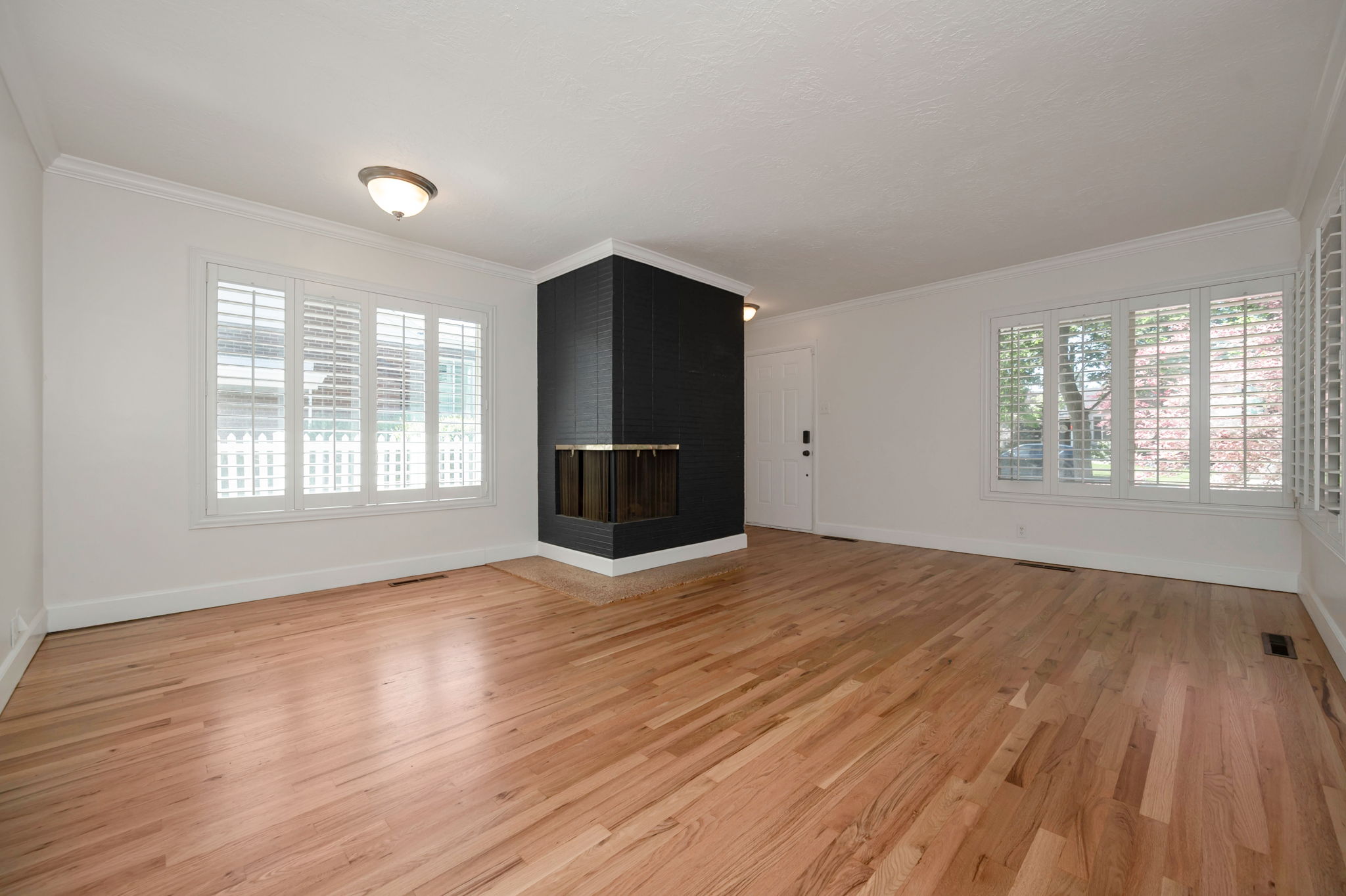 Spacious room featuring wood-finish flooring, a corner fireplace, and multiple windows with white plantation shutters