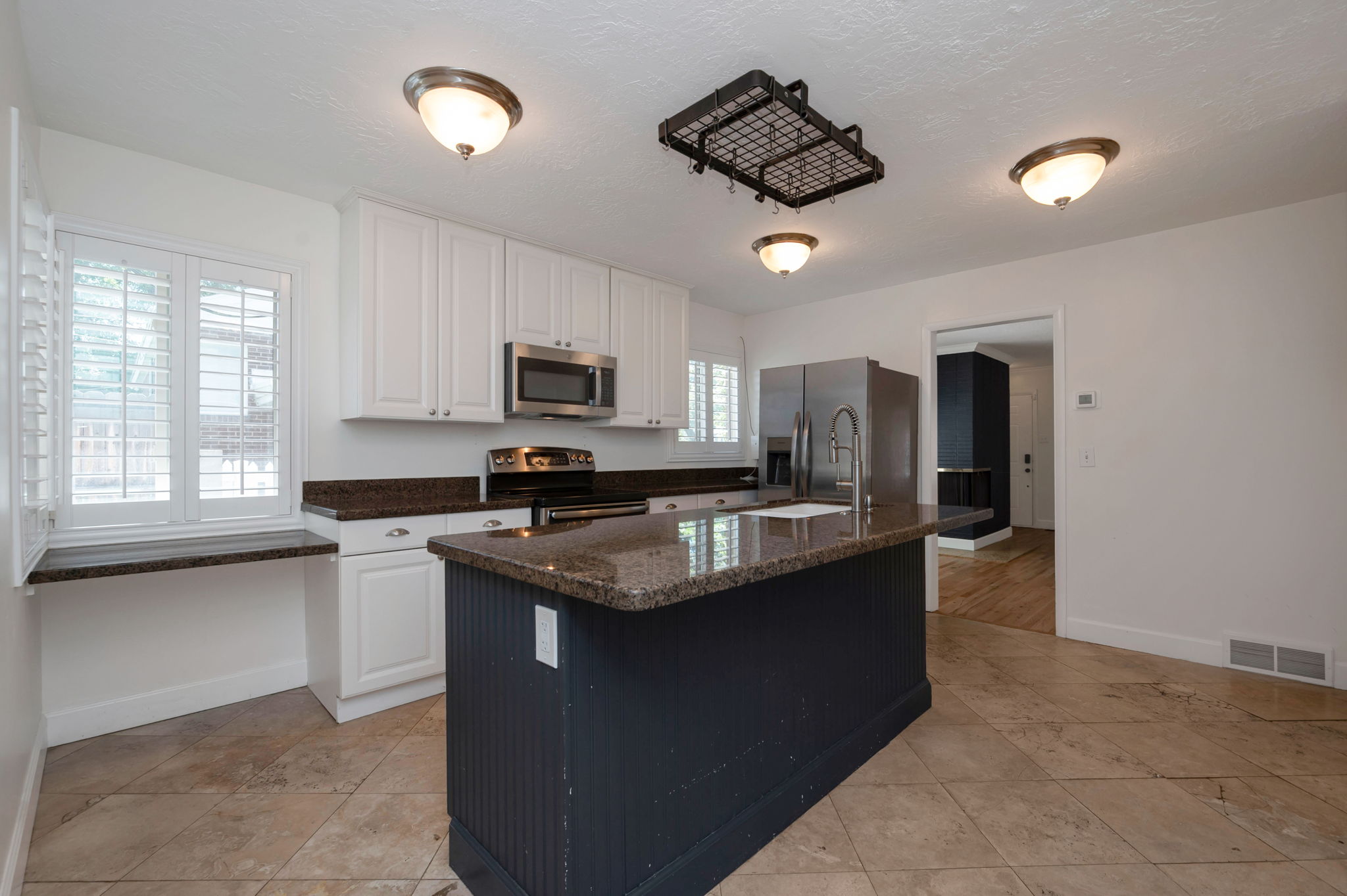 Kitchen featuring a dark-toned central island with a granite-style countertop and integrated sink, white upper and lower cabinetry, stainless steel appliances, and ceiling-mounted flush light fixtures