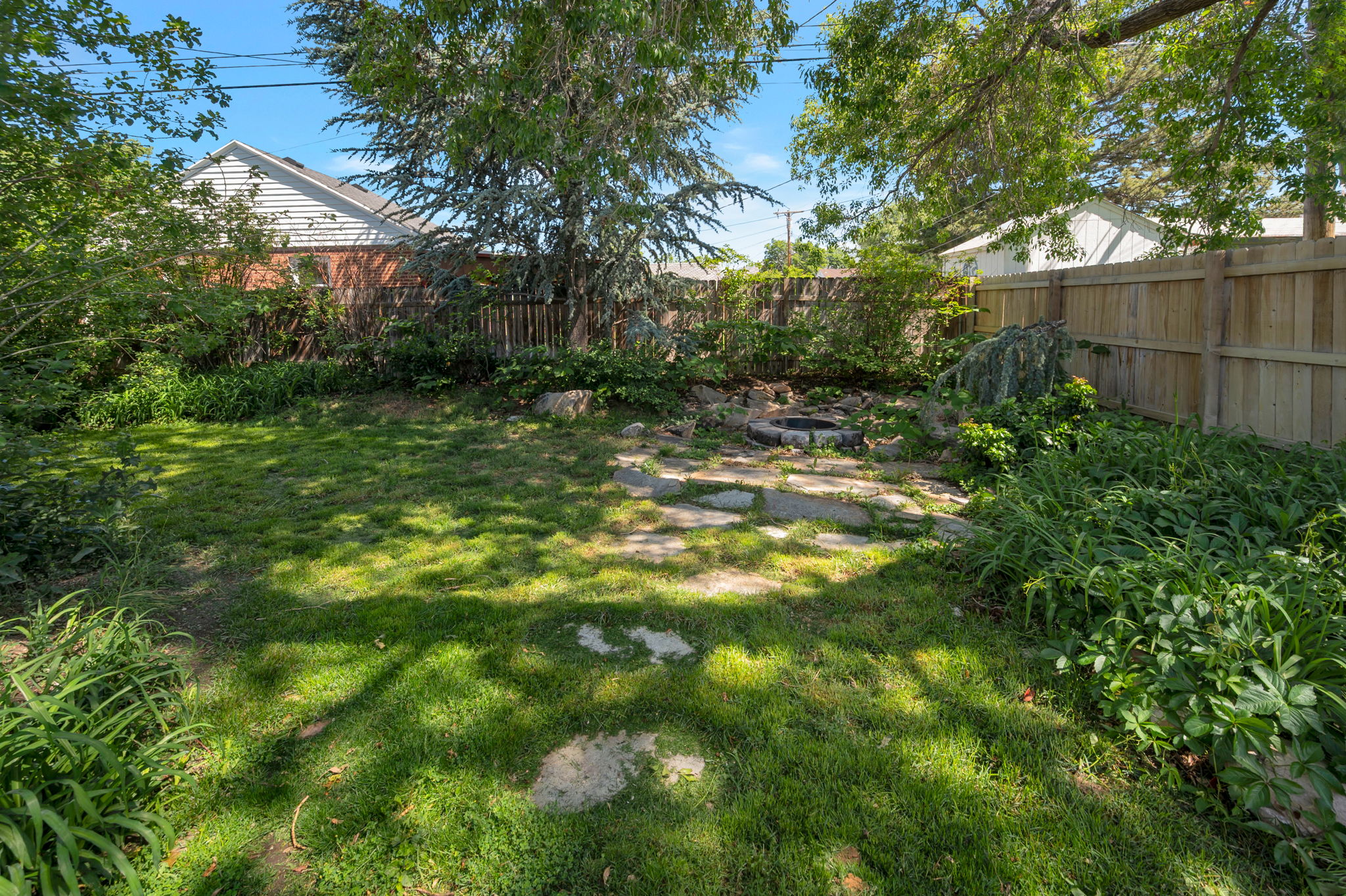 Grassy backyard area featuring a partial stone path, mature trees, and privacy fencing
