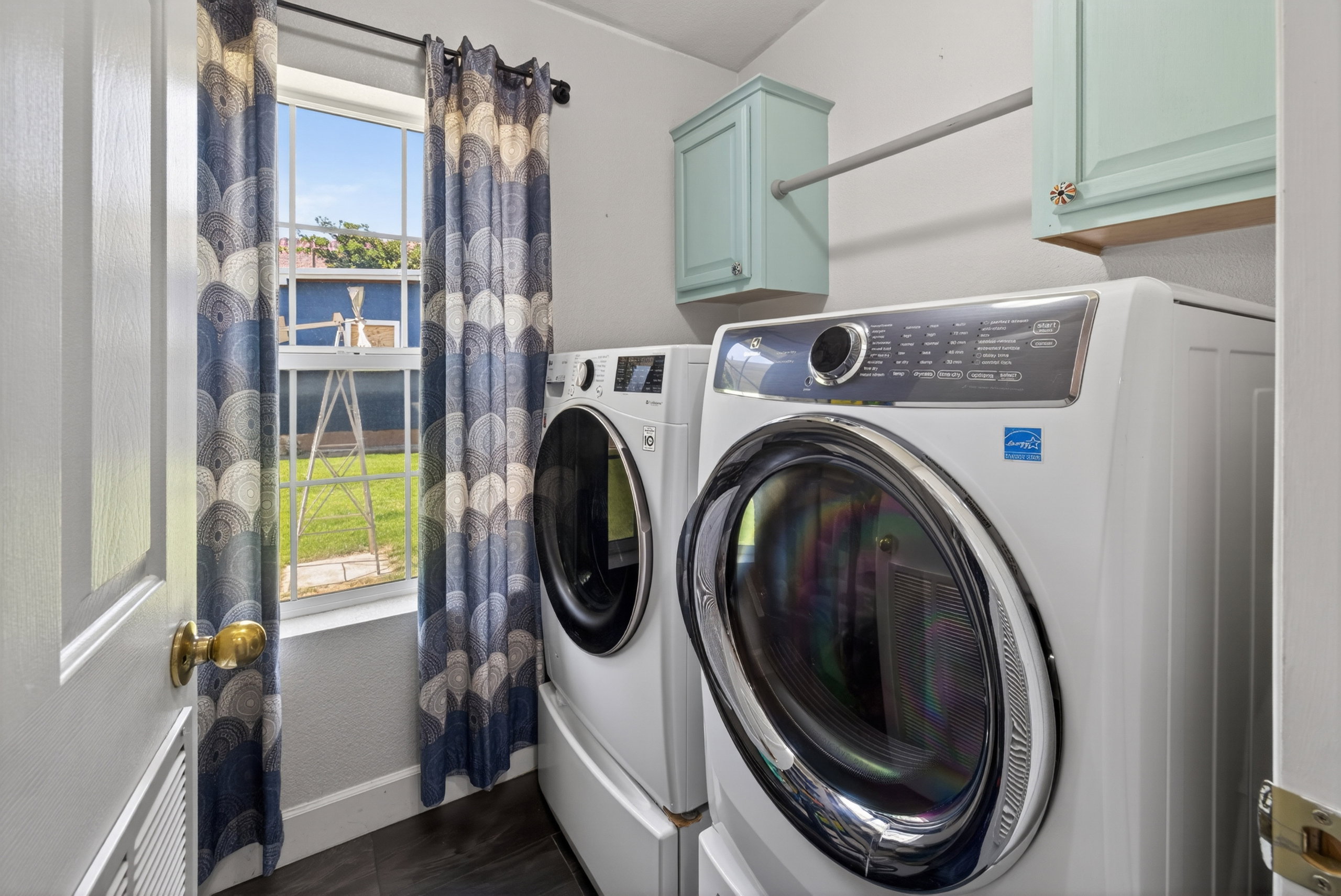 Dedicated laundry area featuring a window, wood-finish flooring, two wall-mounted cabinets, and a clothing rod