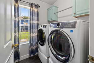 Dedicated laundry area featuring a window, wood-finish flooring, two wall-mounted cabinets, and a clothing rod