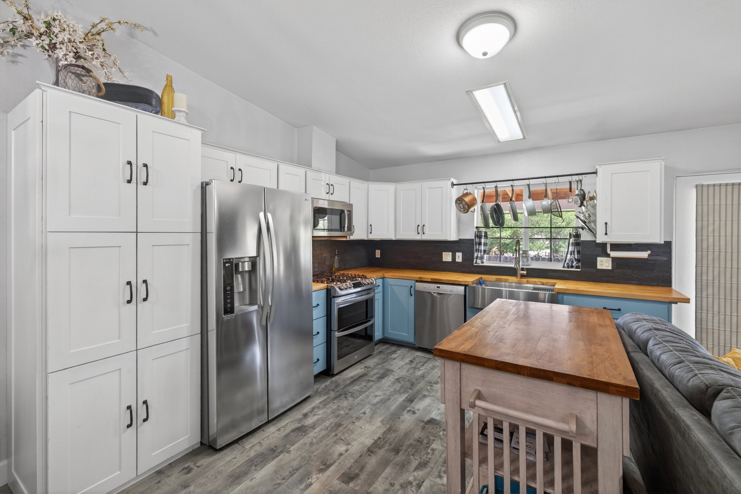 Modern kitchen featuring white upper cabinetry, blue lower cabinetry, stainless steel appliances, wood-finish countertops, and wood-finish flooring