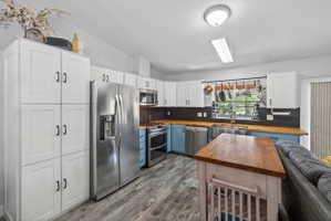 Modern kitchen featuring white upper cabinetry, blue lower cabinetry, stainless steel appliances, wood-finish countertops, and wood-finish flooring