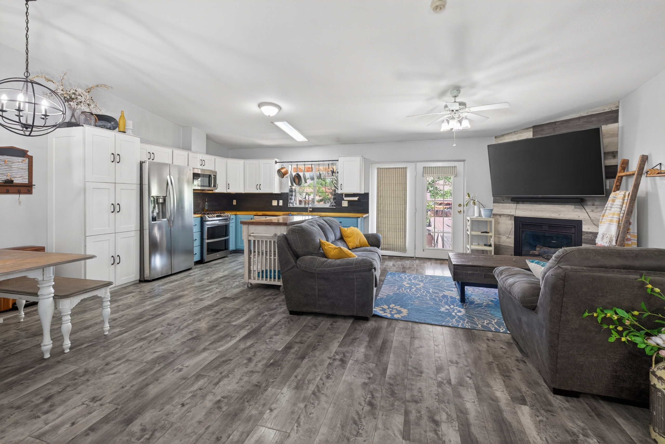 Spacious open-concept living area featuring wood-finish flooring, a corner fireplace with a shiplap accent wall, and a ceiling fan
